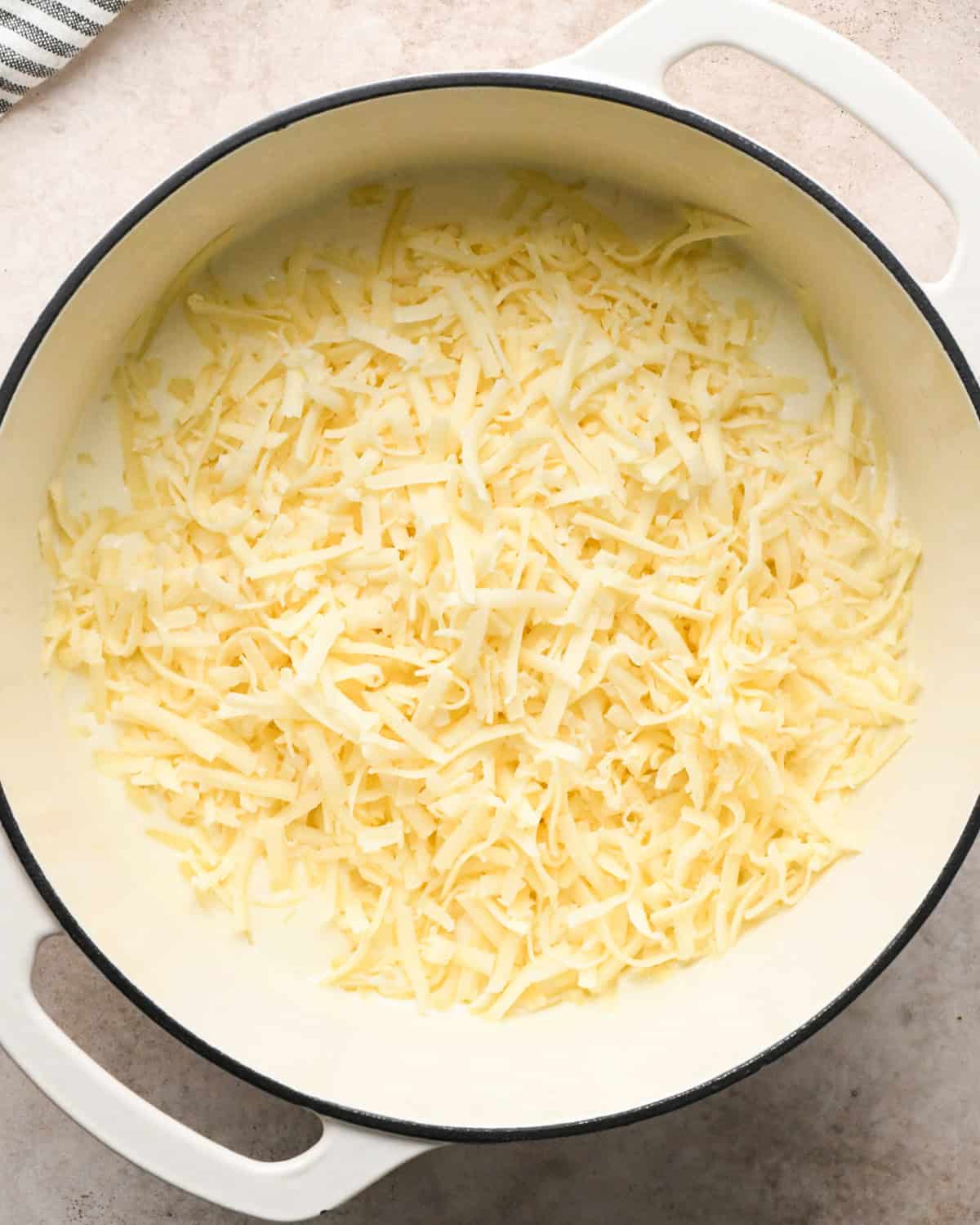 Making broccoli macaroni and cheese (mac and cheese): overhead photo of shredded cheese being added to homemade cheese sauce in a large pot.