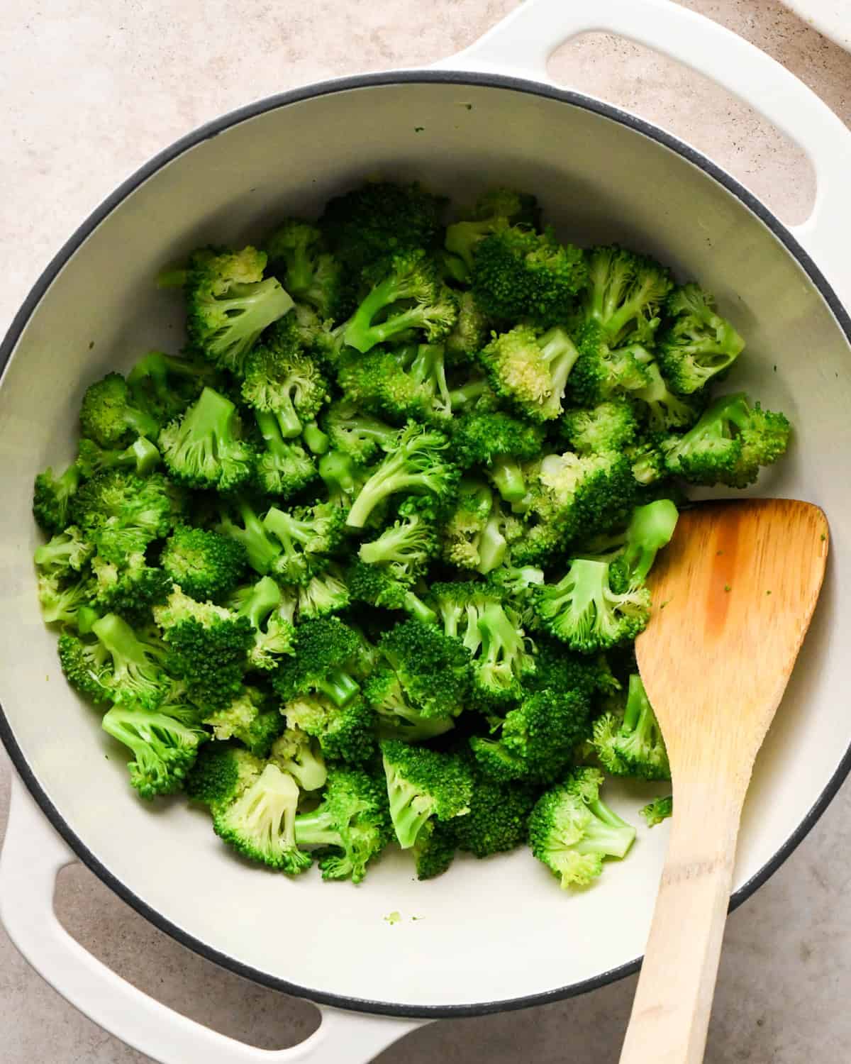 Making broccoli macaroni and cheese (mac and cheese): overhead photo of broccoli florets added to a large pot and being sautéed with a wooden spoon.