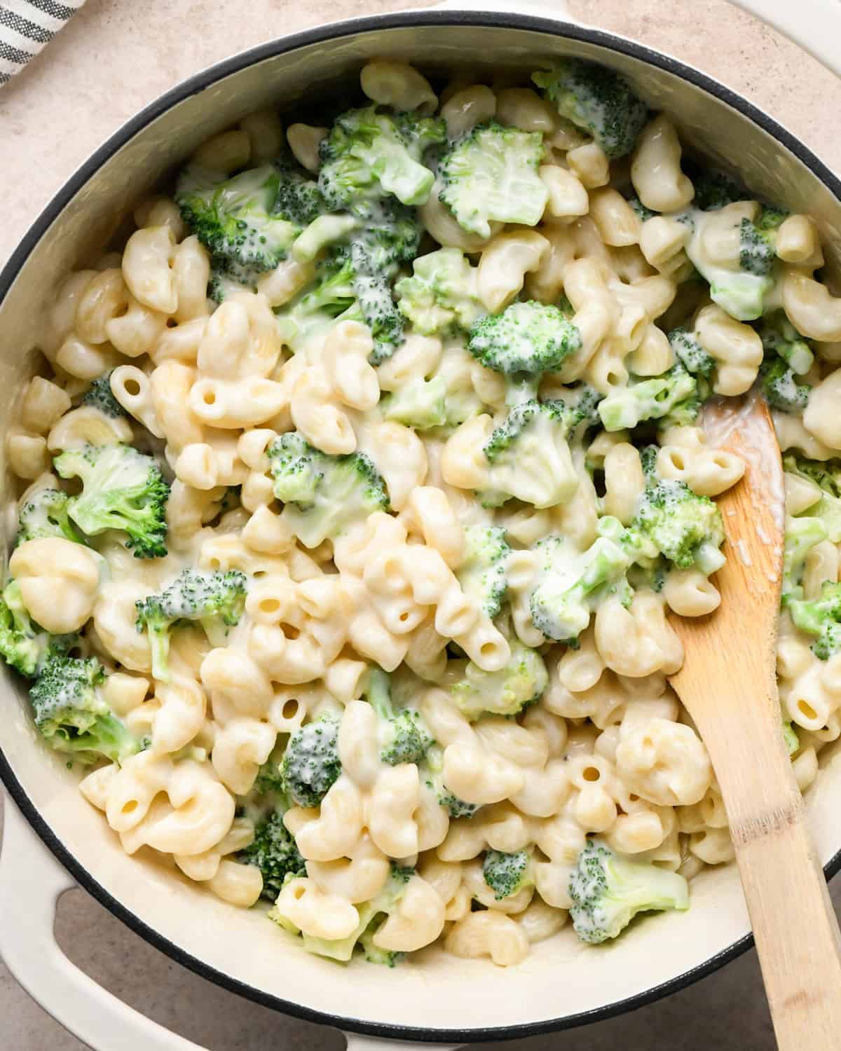 Making broccoli macaroni and cheese (mac and cheese): overhead photo of cooked broccoli, elbow pasta, and homemade cheese sauce combined in a large pot and being stirred with a wooden spoon.