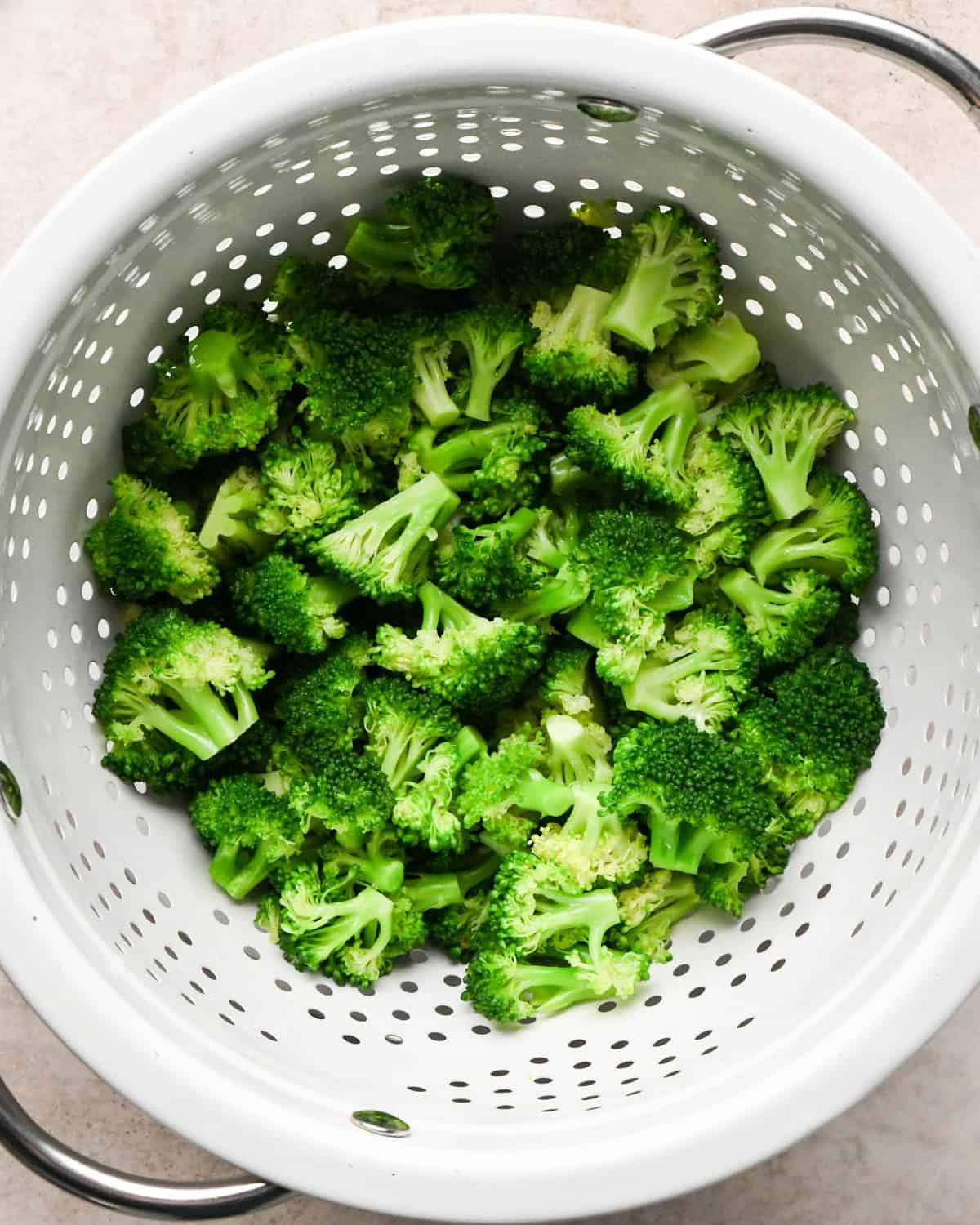 Making broccoli macaroni and cheese (mac and cheese): overhead photo of sautéed broccoli florets poured into a white colander to drain the water.
