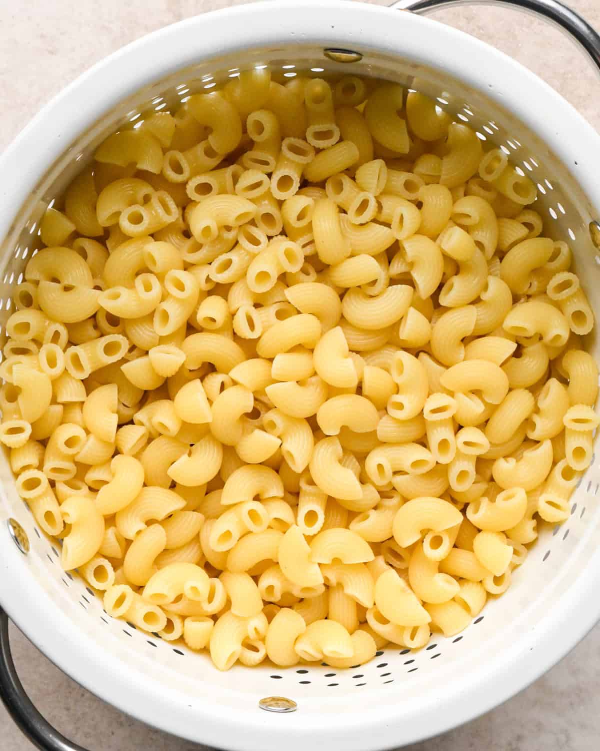 Making broccoli macaroni and cheese (mac and cheese): overhead photo of cooked elbow pasta being drained in a white colander.