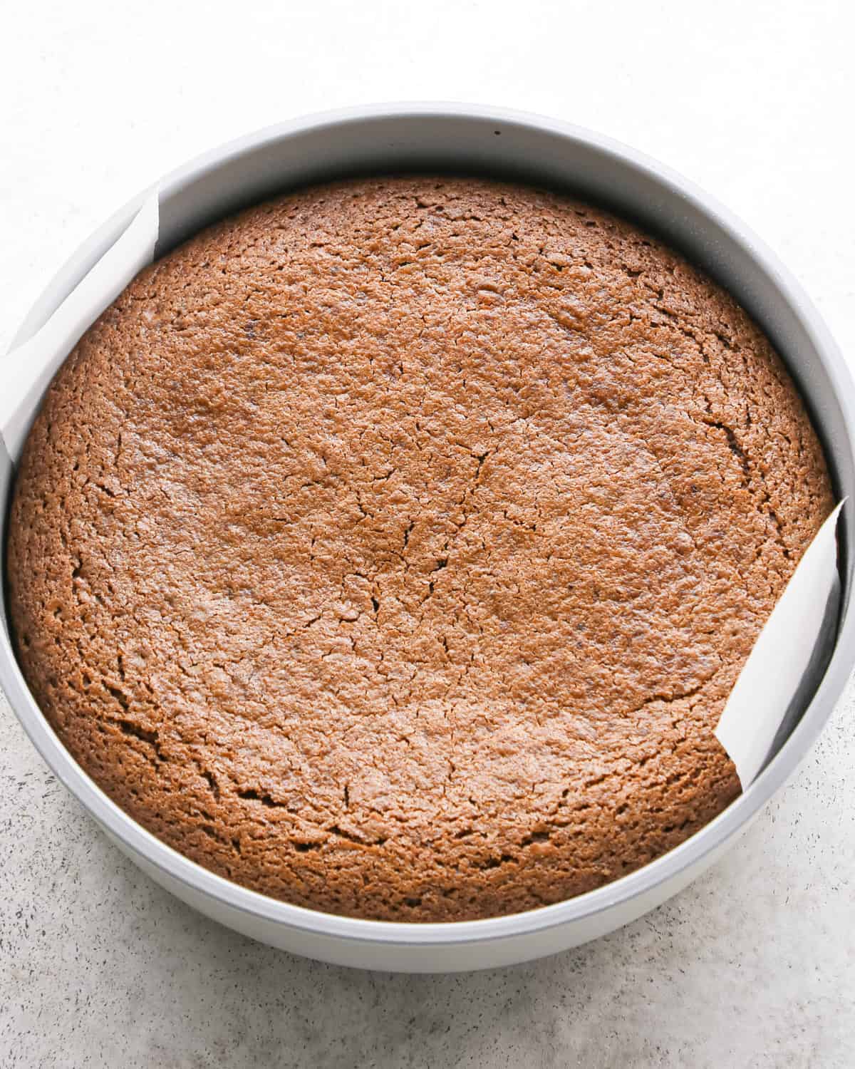 olive oil chocolate cake in a round, silver cake pan after baking