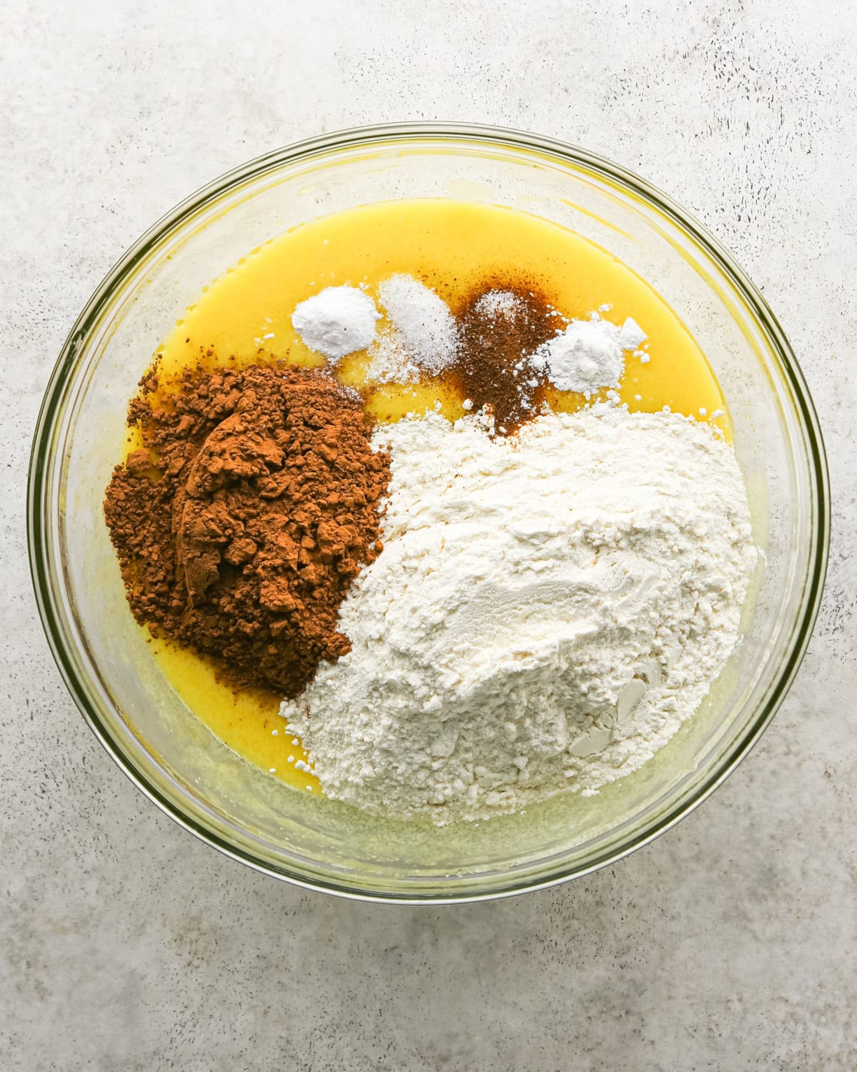 making chocolate olive oil cake - flour, cocoa powder, sea salt, baking soda, baking powder and espresso powder added to the wet ingredients in a glass bowl before whisking