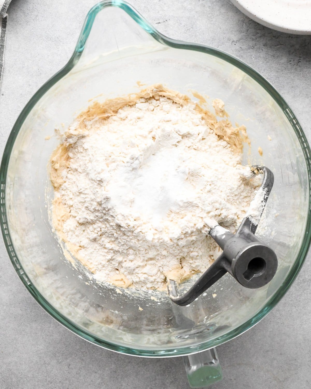 making cookie dough brownies - dry ingredient mixture added to the wet ingredient mixture in a glass mixing bowl with the paddle attachment int he bowl before mixing