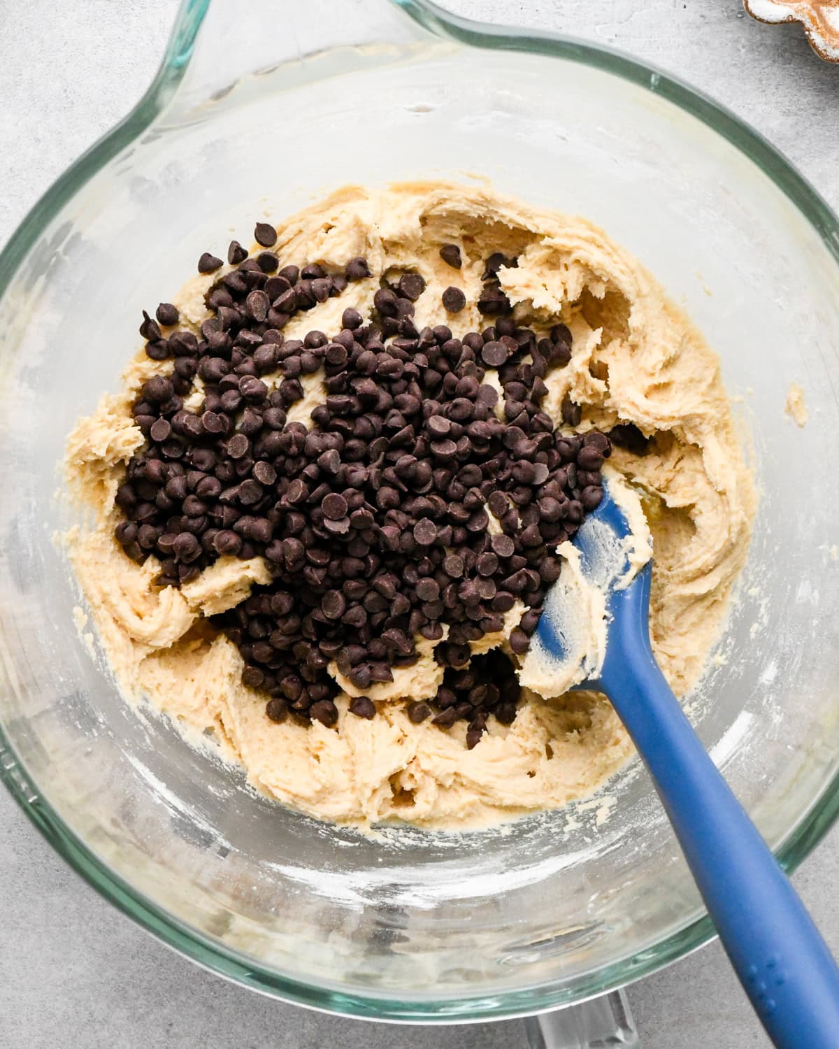 making cookie dough brownies - chocolate chips added to the cookie dough in a glass mixing bowl with a blue spatula.