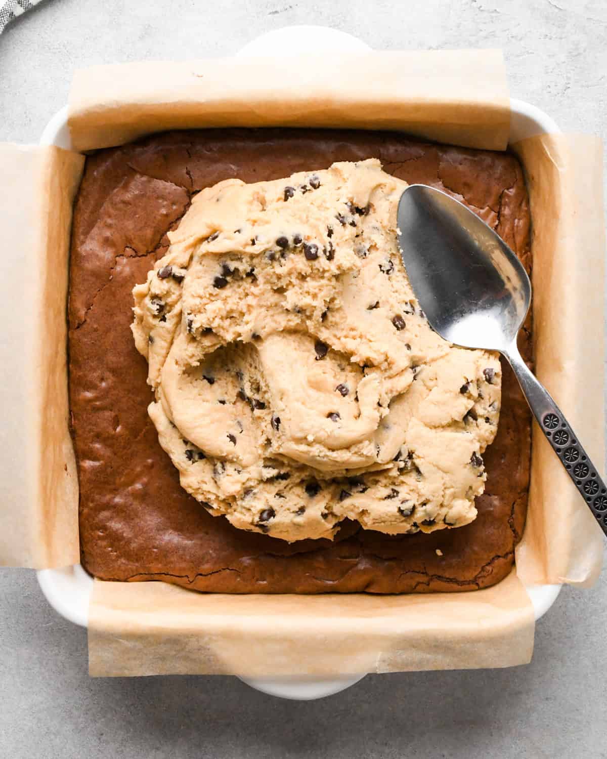 assembling cookie dough brownies - a silver spoon beginning to spread cookie dough over the brownie layer