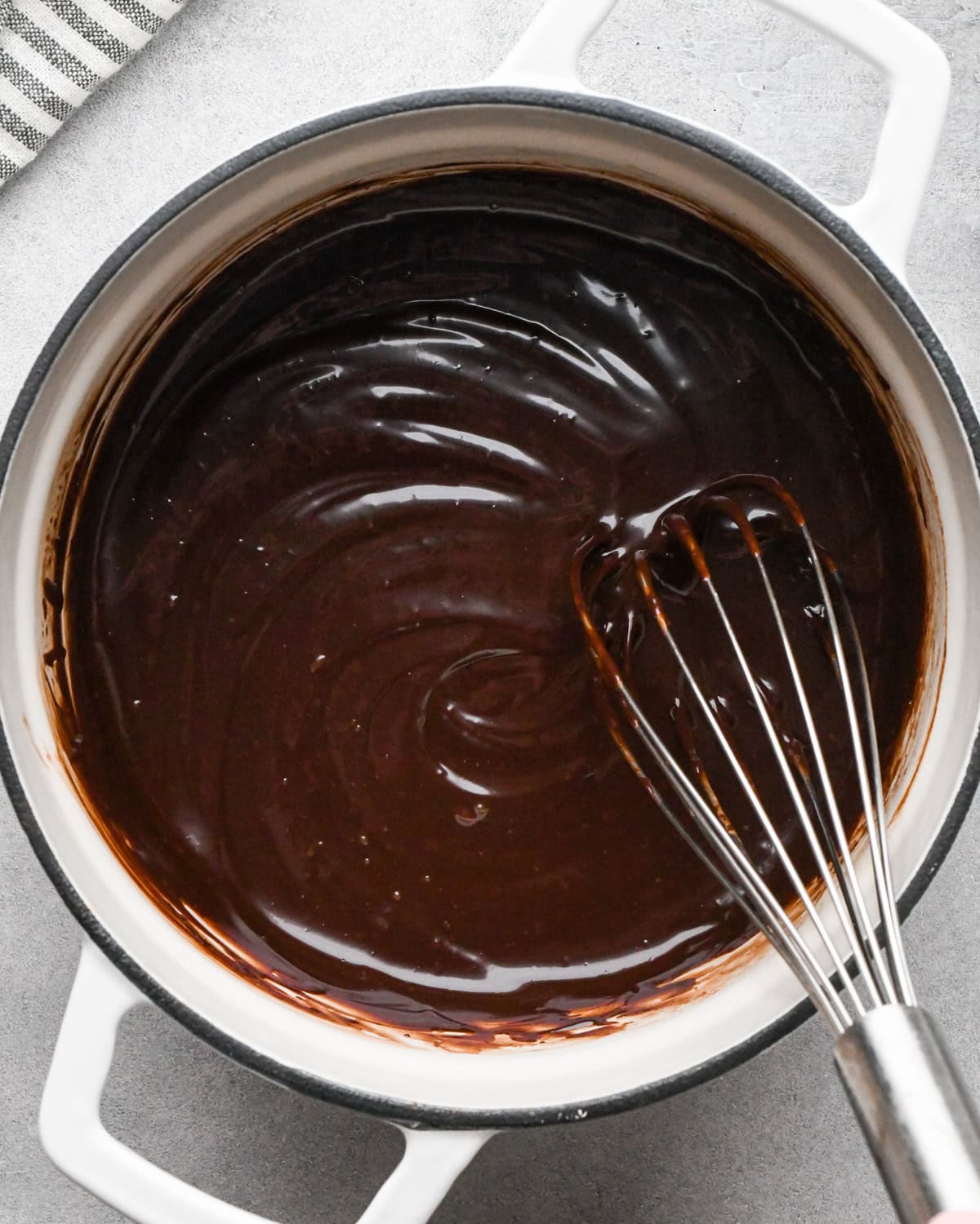 chocolate ganache for cookie dough brownies in a white pot with a whisk stirring the ganache