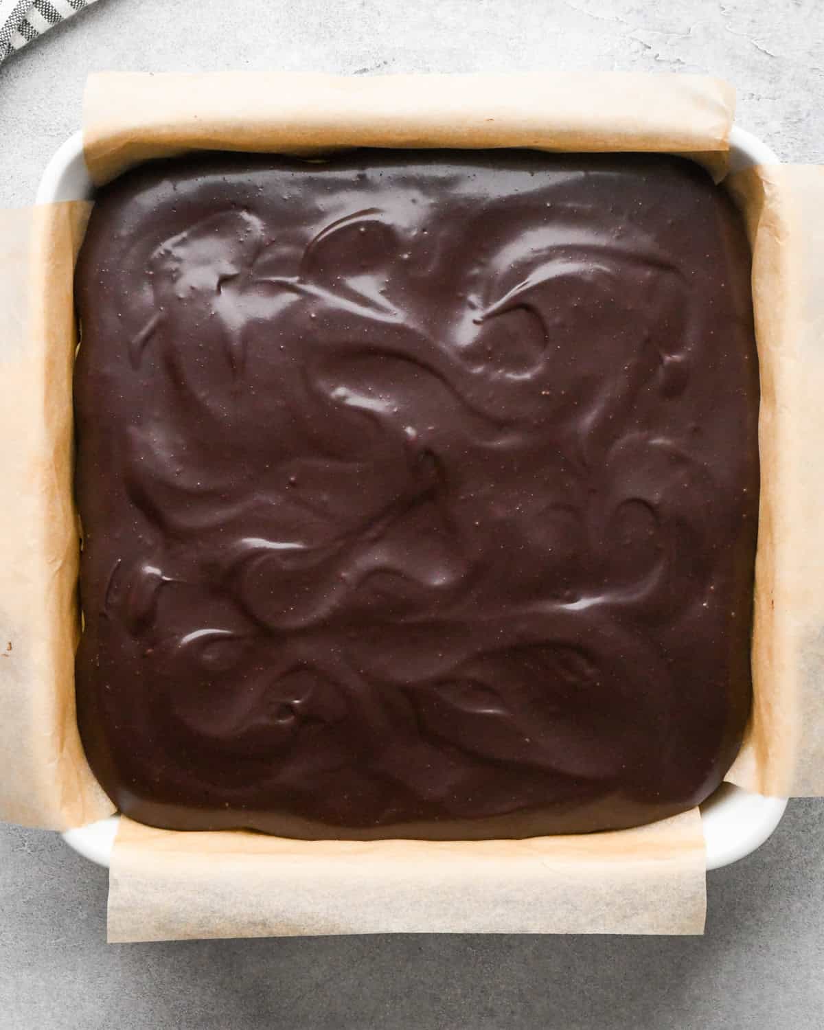chilled cookie dough brownies in a white ceramic square baking dish lined with parchment paper