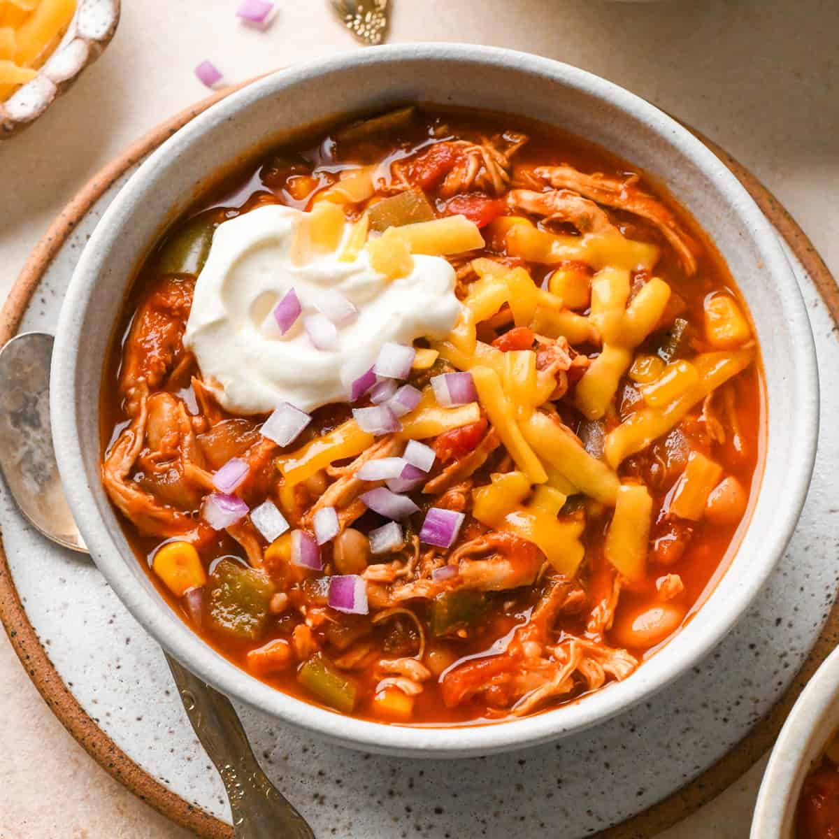 a bowl of Slow Cooker Chicken Chili with sour cream, cheese and red onions on top