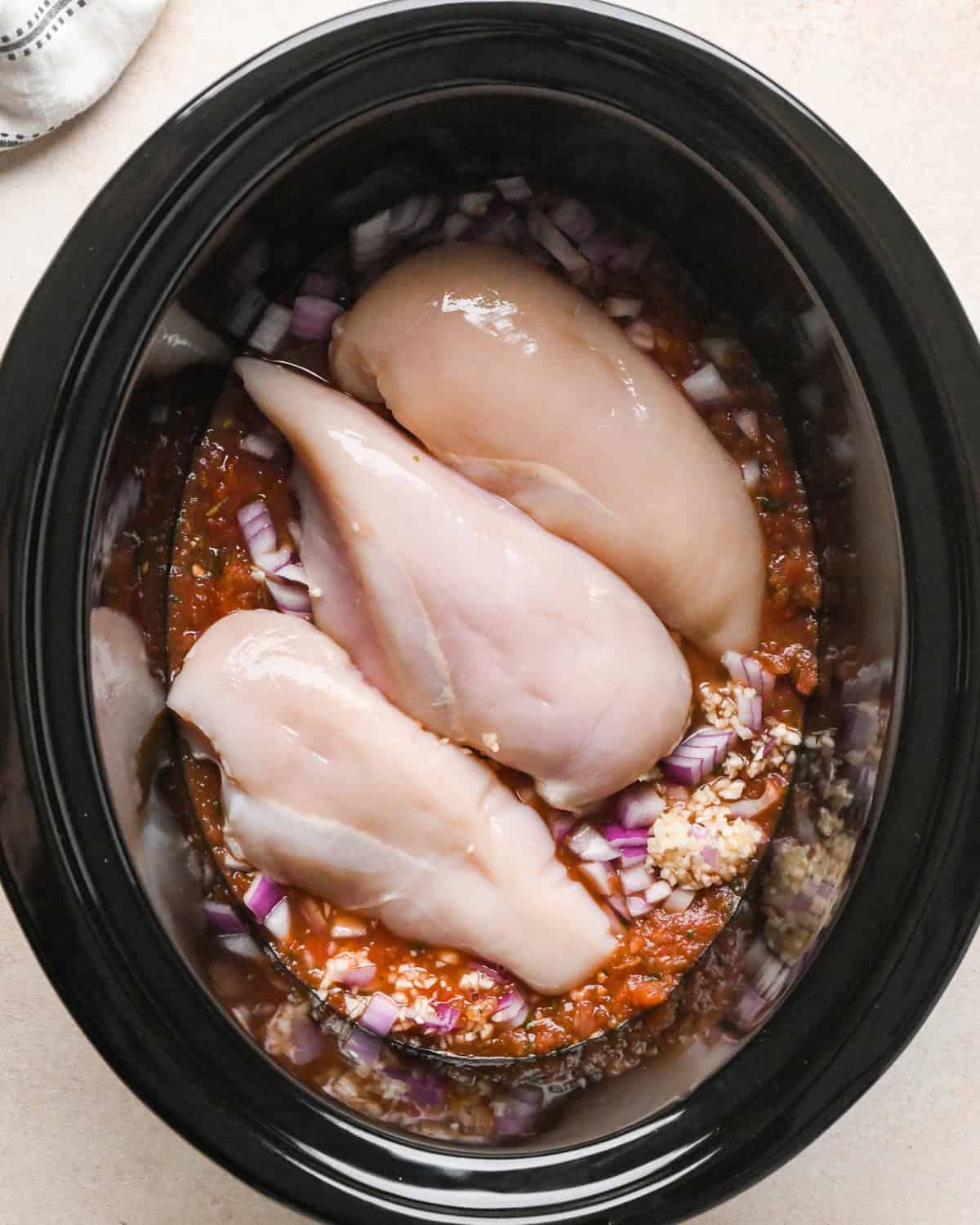 three large chicken breasts in a crock pot with salsa, onions and garlic before cooking, making Slow Cooker Chicken Chili