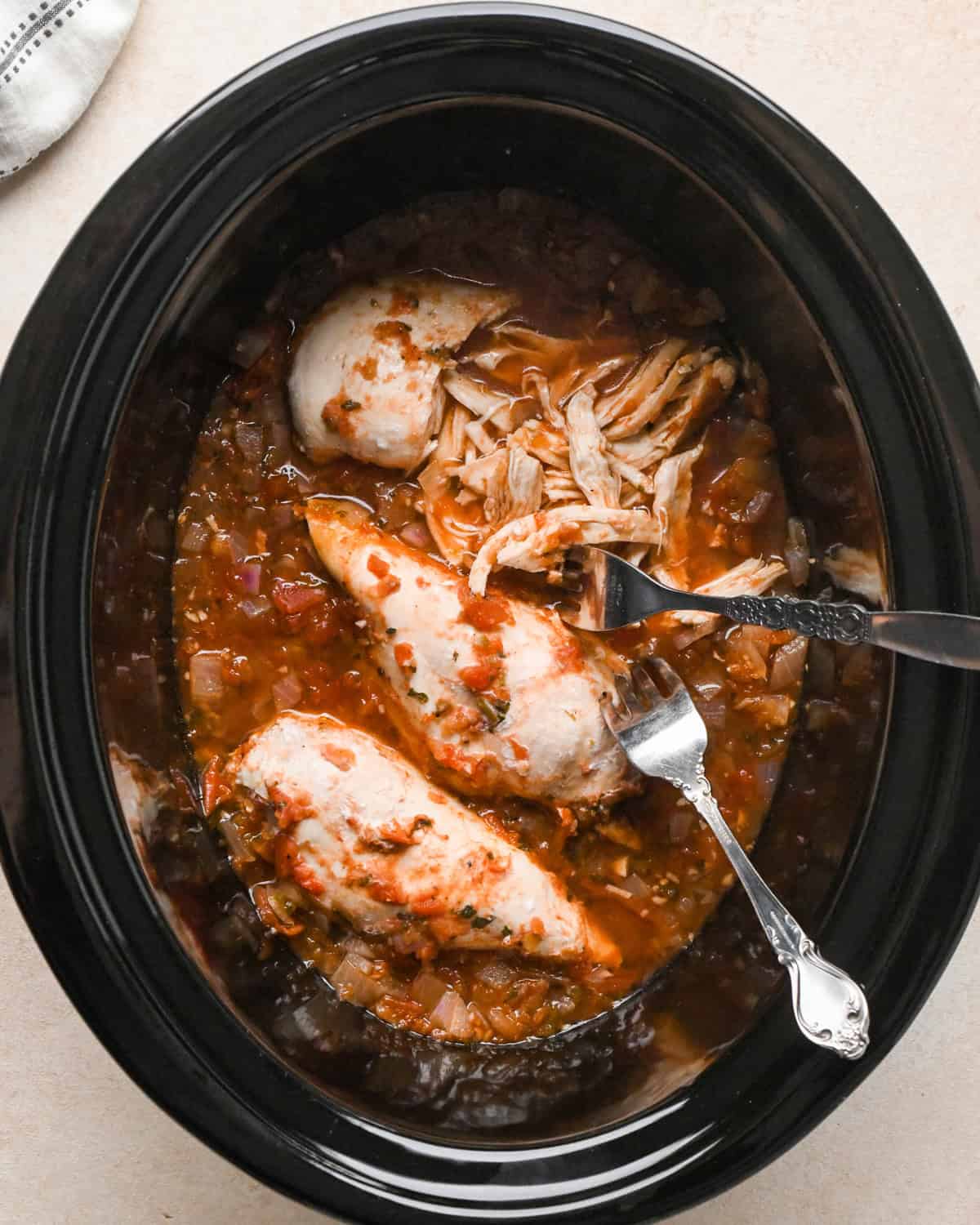 two forks shredding chicken breasts in a slow cooker making Slow Cooker Chicken Chili