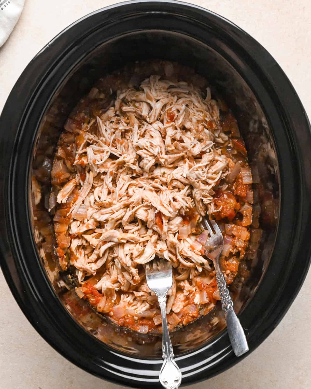 shredded chicken with two forks in the container of a slow cooker with salsa