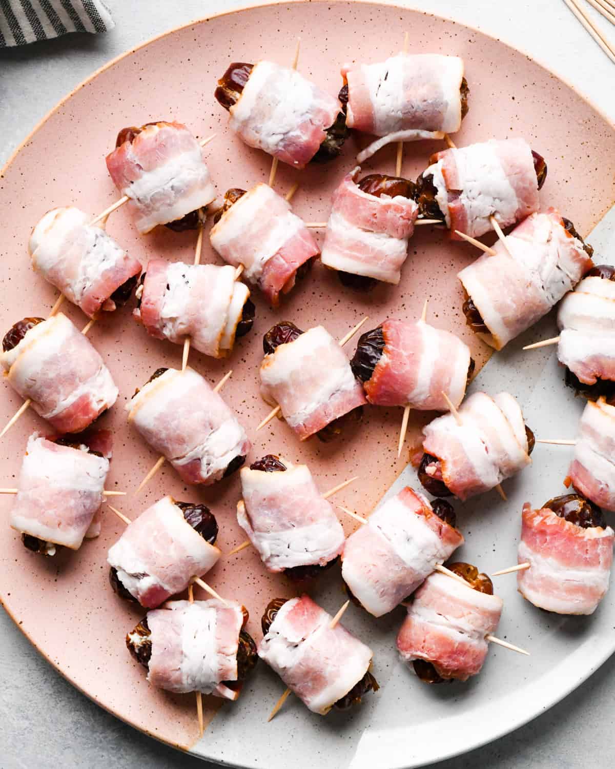 Making bacon-wrapped dates: overhead photo of bacon-wrapped dates, each one secured with a toothpick and arranged on a speckled plate.