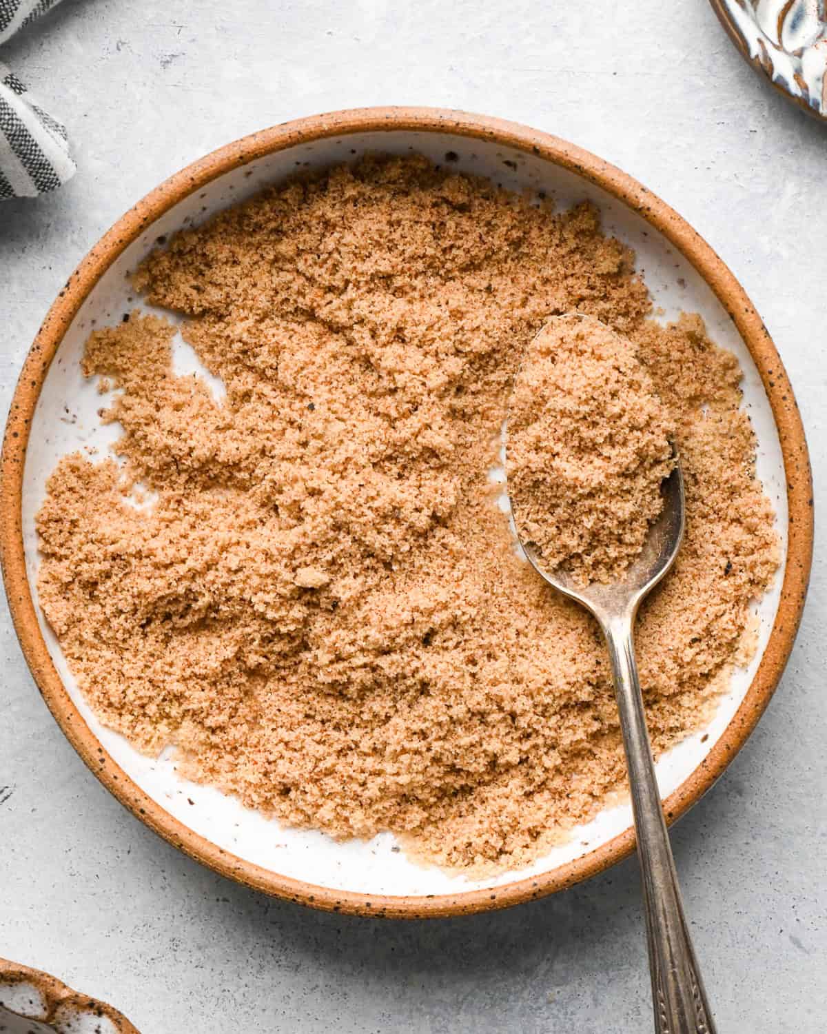 Making bacon-wrapped dates: overhead photo of brown sugar, paprika, pepper, and garlic powder on a white speckled plate and mixed together with a spoon.