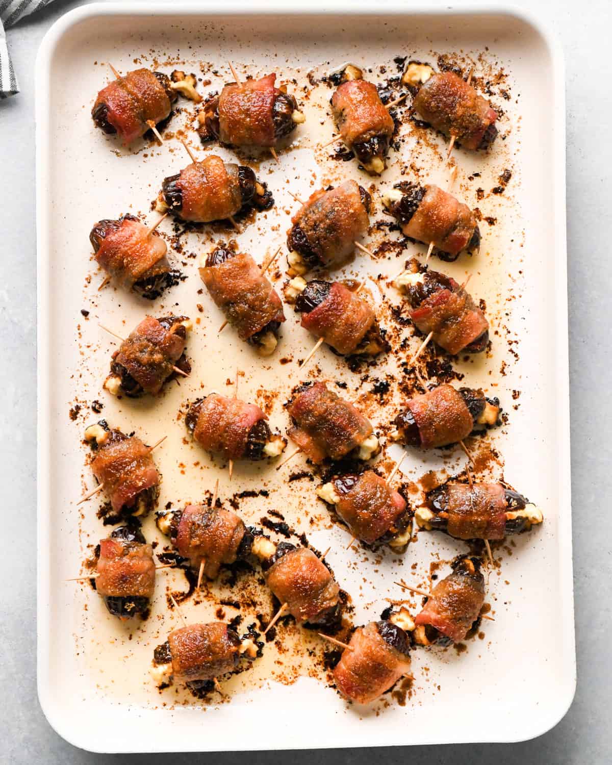 Making bacon-wrapped dates: overhead photo of completed bacon-wrapped dates topped with brown sugar topping and cooked on a light-colored cooking sheet.
