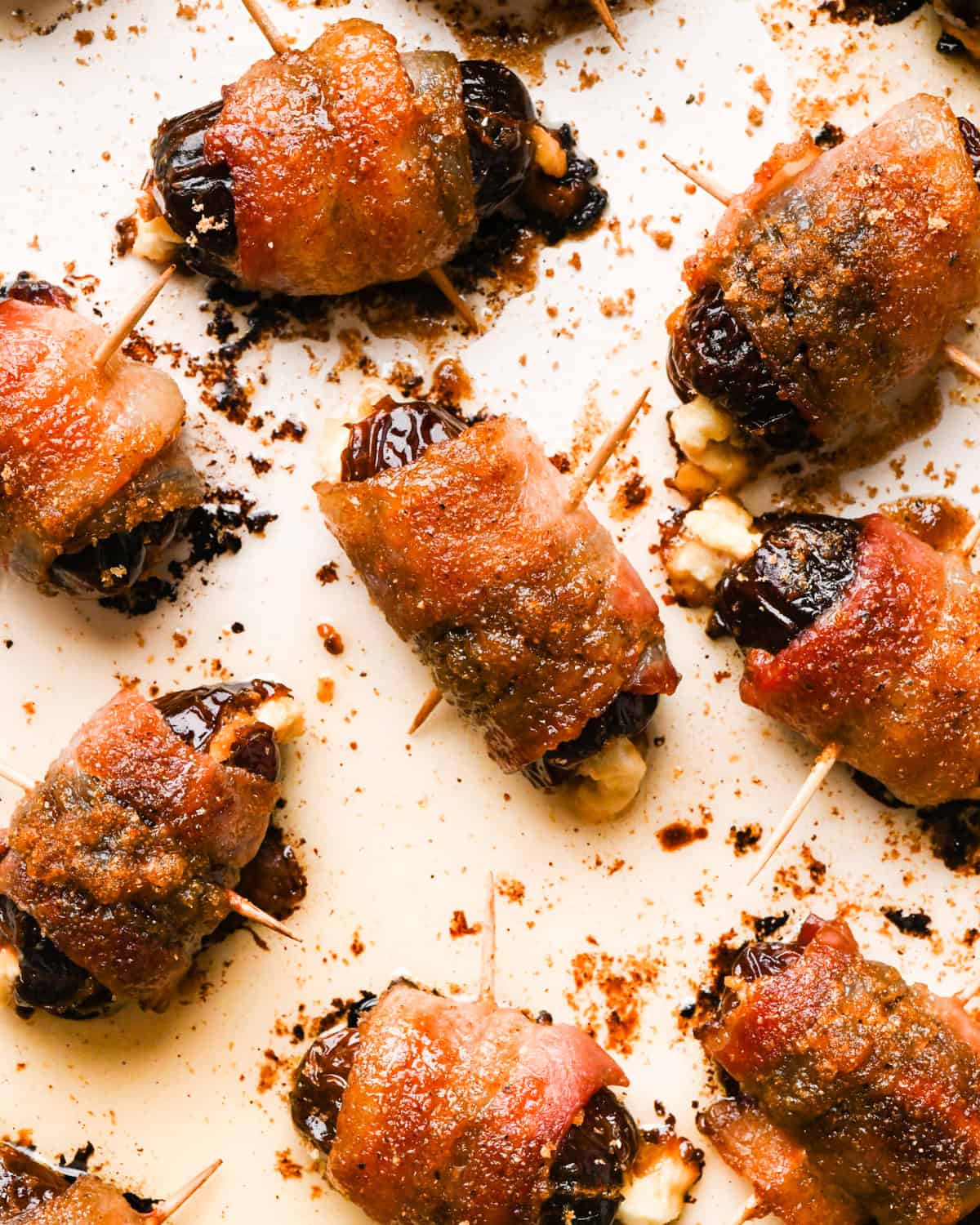 Making bacon-wrapped dates: close-up photo of completed bacon-wrapped dates topped with brown sugar topping and cooked on a light-colored cooking sheet.