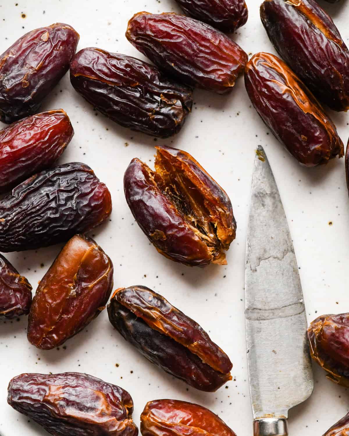 Making bacon-wrapped dates: overhead photo of dates arranged on a white speckled plate with one of the dates cut in half and a knife sitting on the plate.