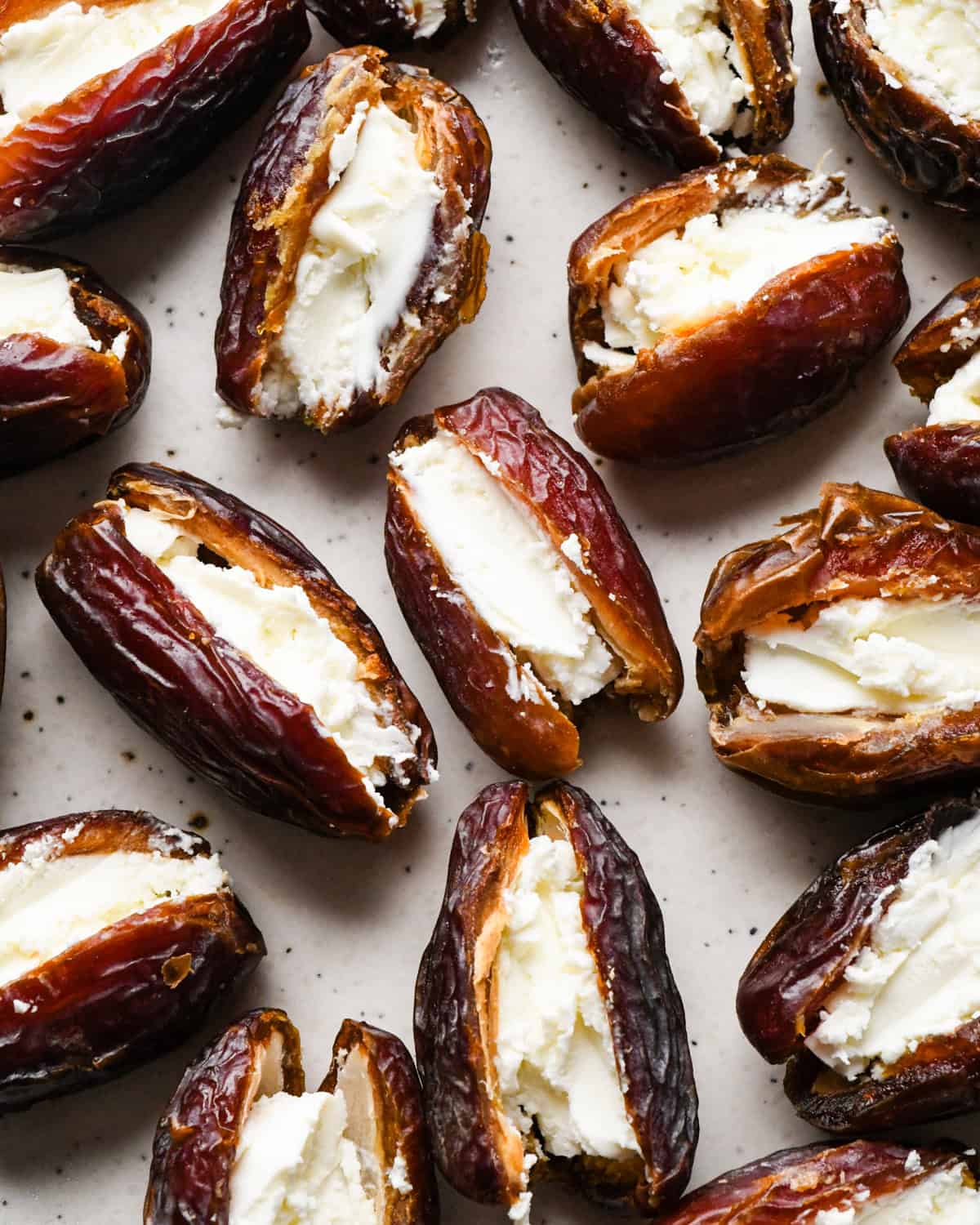 Making bacon-wrapped dates: overhead photo of dates arranged on a white speckled plate. Each date has been filled with goat cheese.