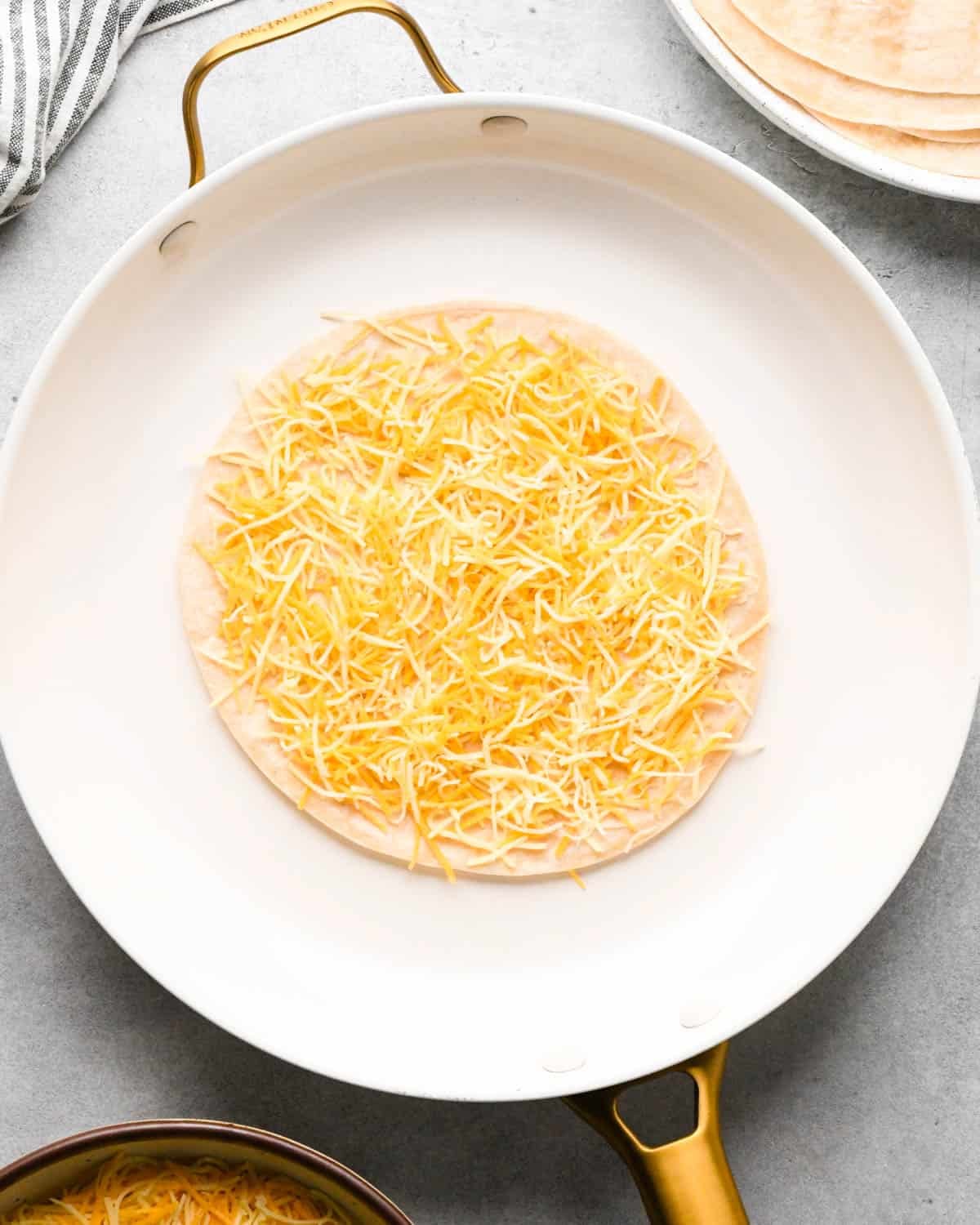 making breakfast quesadillas - a tortilla topped with Mexican blend cheese in a white skillet
