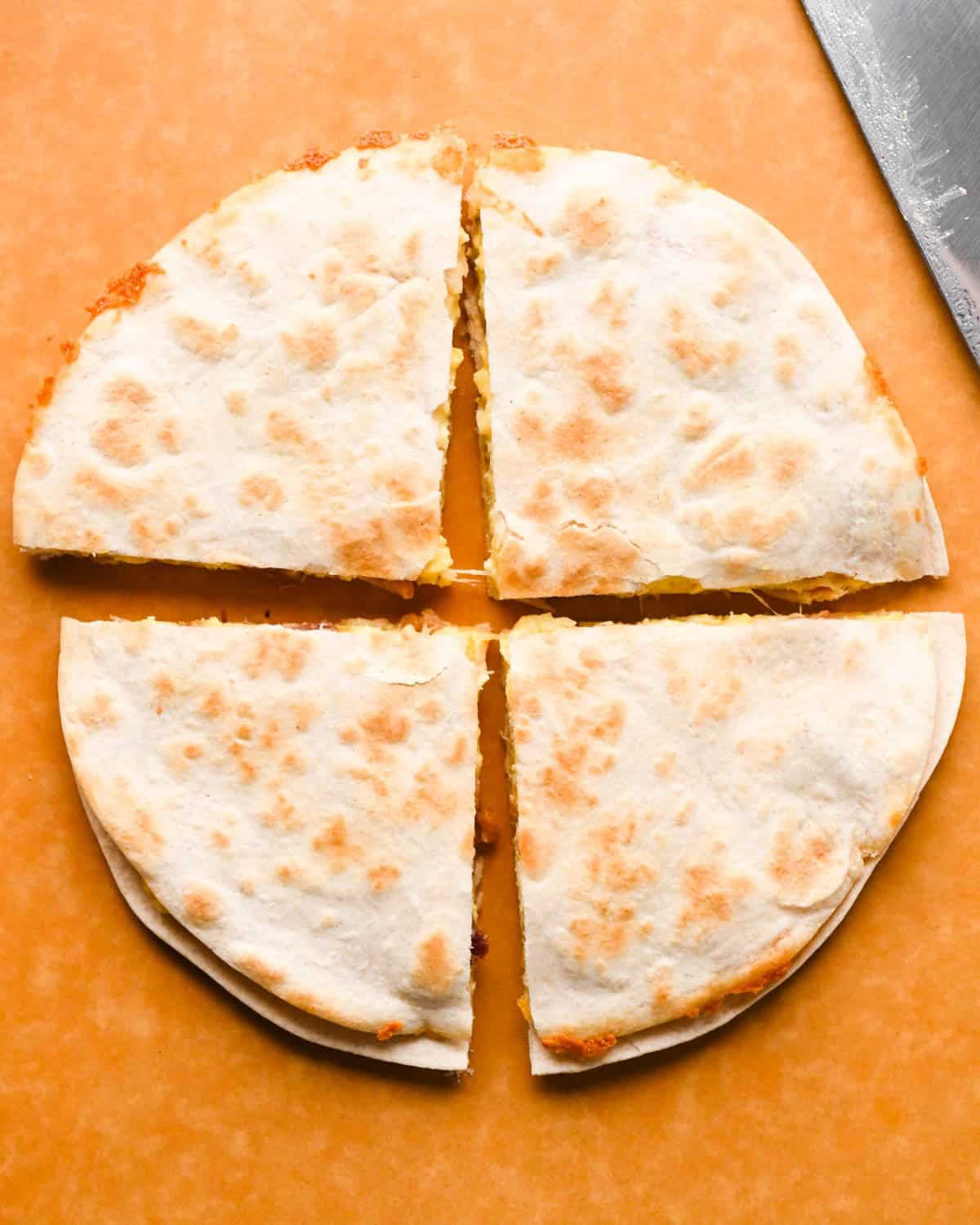 a breakfast quesadilla into fourths on a brown cutting board
