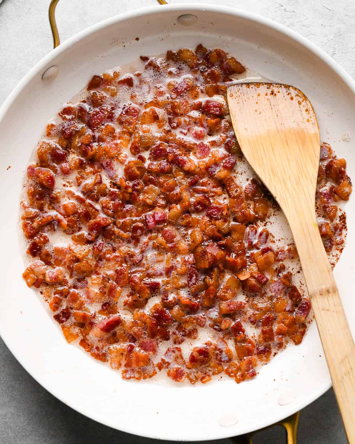 making breakfast quesadillas - cooked diced bacon in a white skillet with a wooden spatula