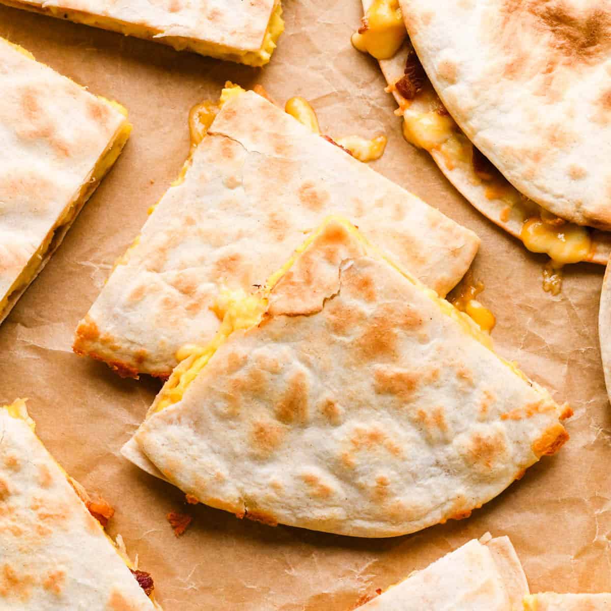 breakfast quesadillas on parchment paper cut into triangles with melty cheese and scrambled eggs inside