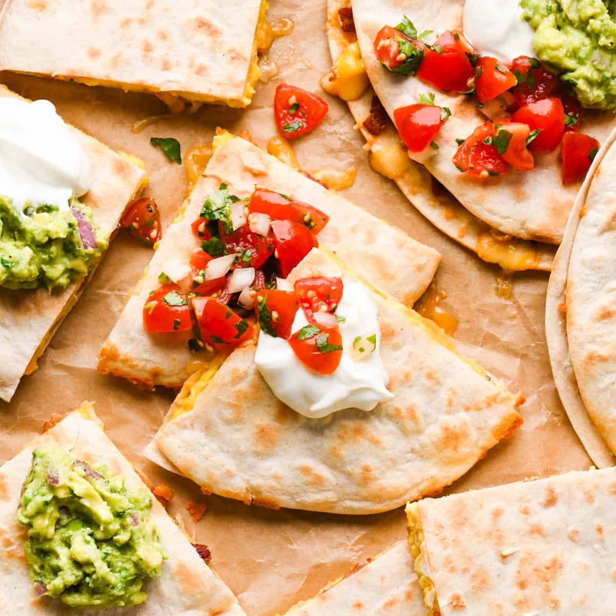 breakfast quesadillas on parchment paper cut into triangles topped with sour cream, pico de gallo and guacamole