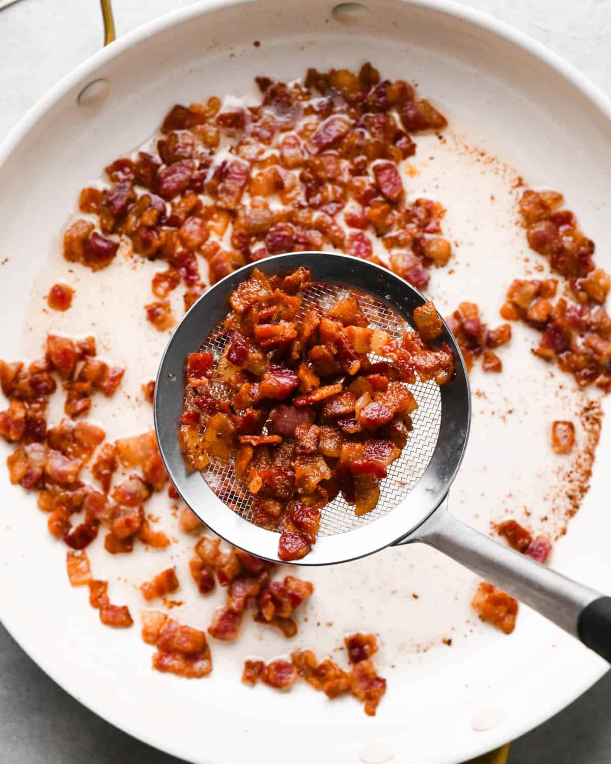 making breakfast quesadillas - a skimmer spoon with some cooked bacon in it being removed from the fry pan