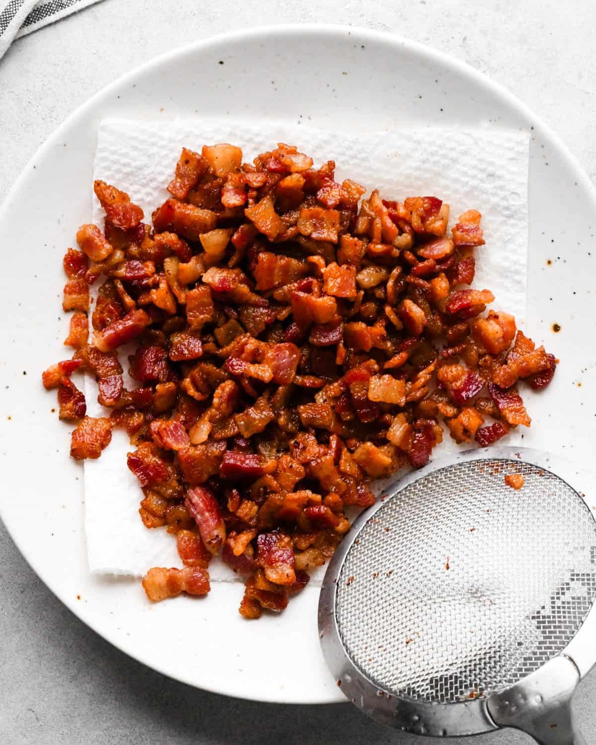 making breakfast quesadillas - cooked diced bacon being put on a paper towel lined plate with a mesh spoon