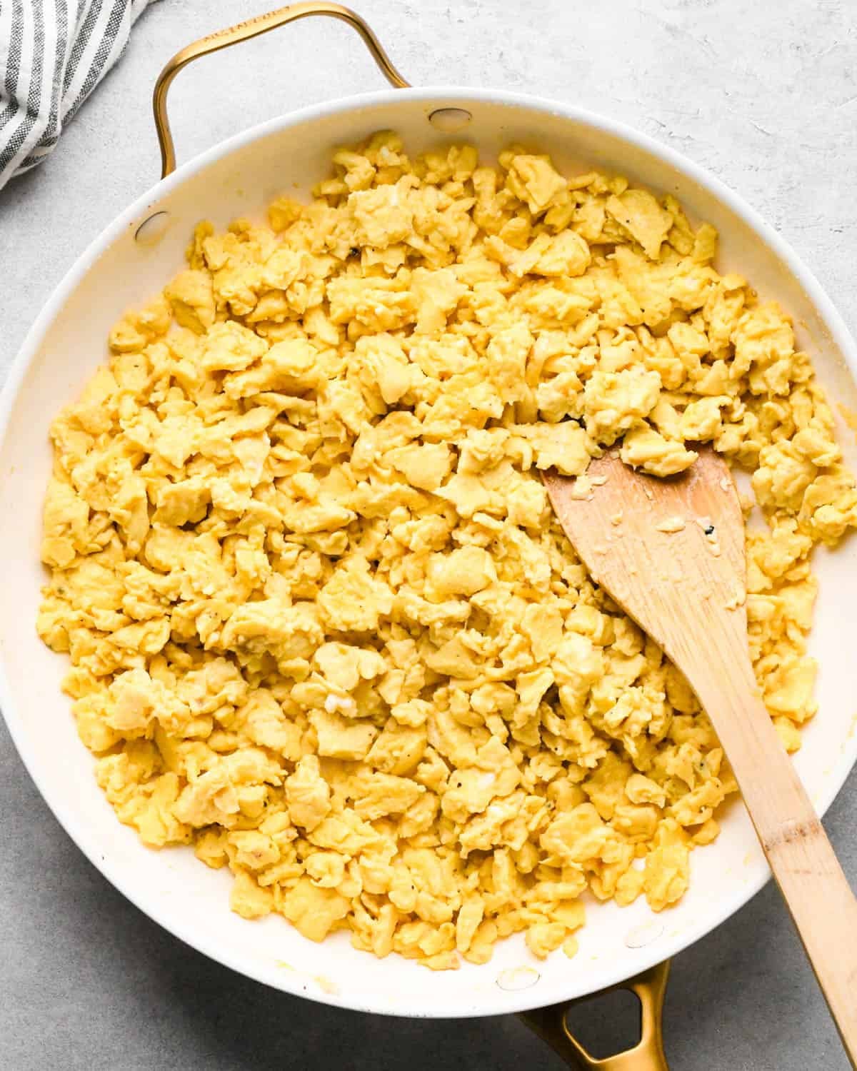 making breakfast quesadillas - cooked scrambled eggs in a white fry pan with a wooden spatula