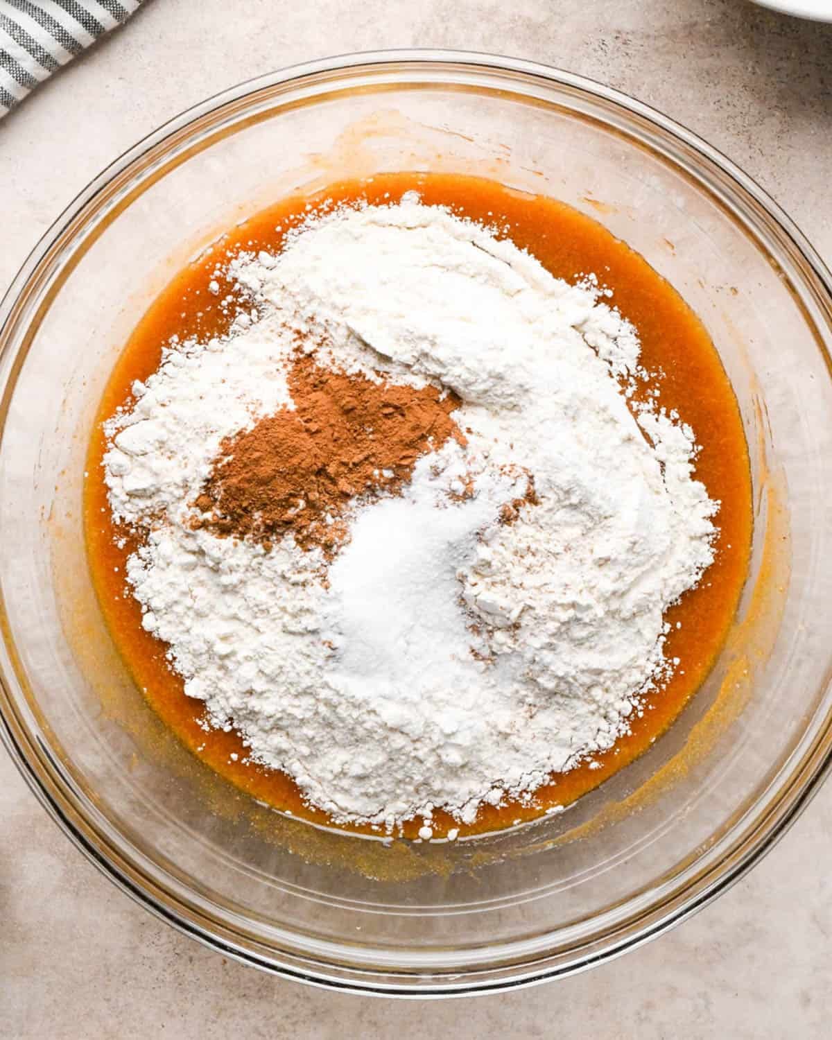 making brown butter pumpkin cookies - flour, baking soda, baking powder, salt, pumpkin pie spice and cinnamon added to the wet ingredients in a class mixing bowl