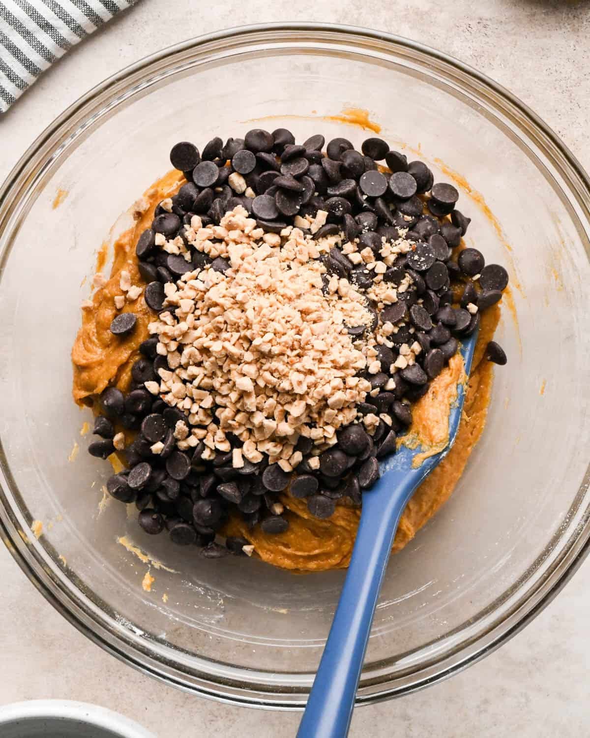 making brown butter pumpkin cookies - chocolate chips and toffee bits added to the dough in a glass mixing bowl with a blue spatula before mixing in