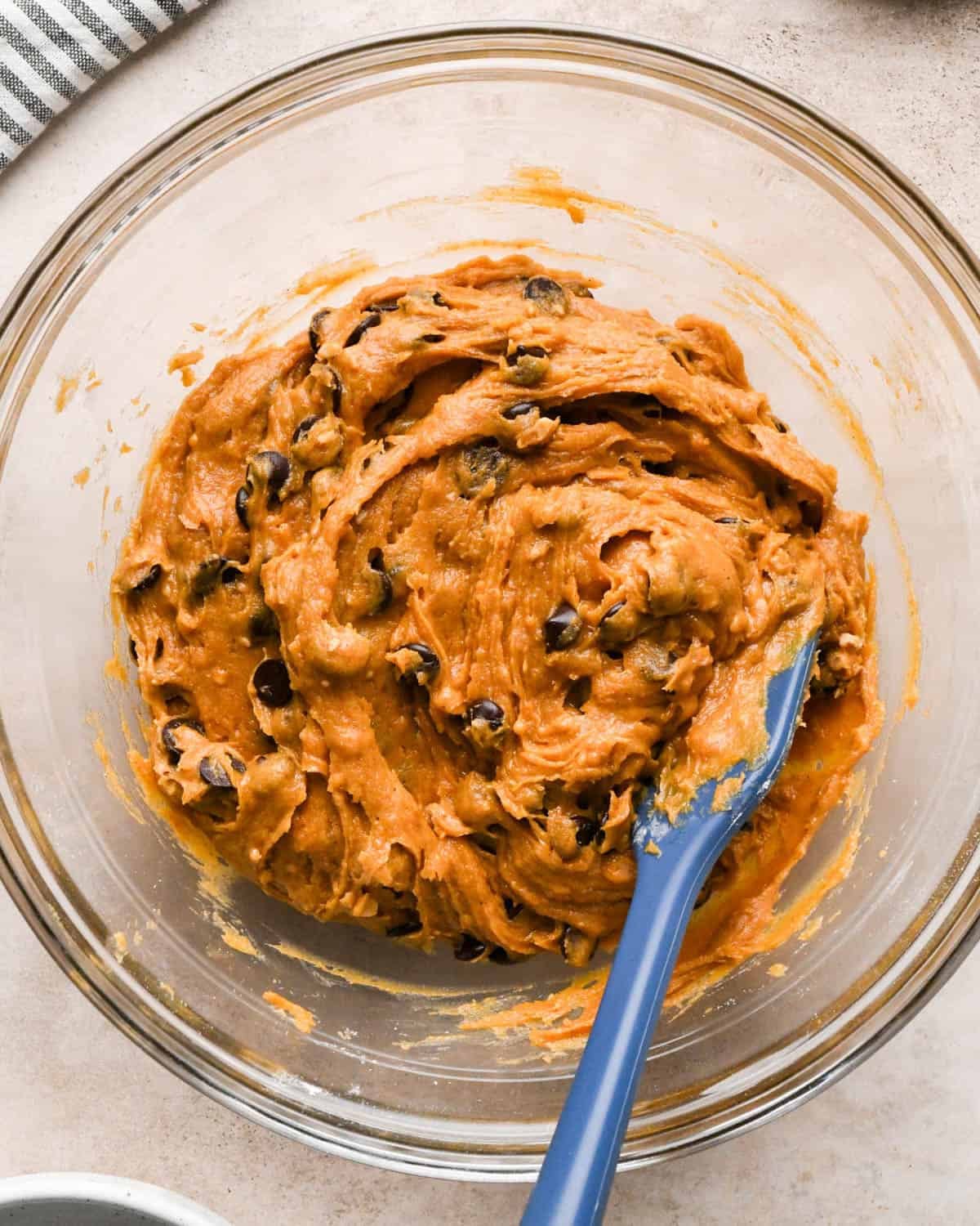 making brown butter pumpkin cookies - dough with the chips and toffee mixed in in a glass bowl with a blue spatula