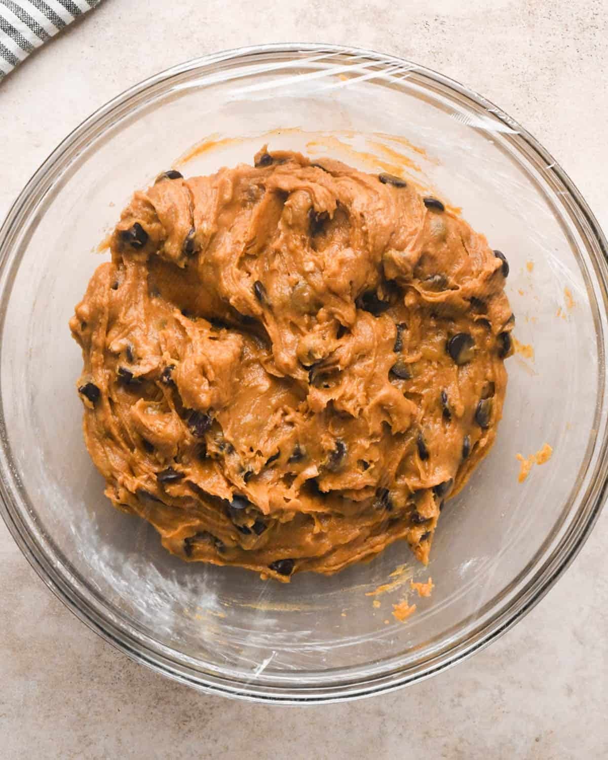 brown butter pumpkin cookie dough in a glass bowl covered in plastic wrap to put in the fridge to chill