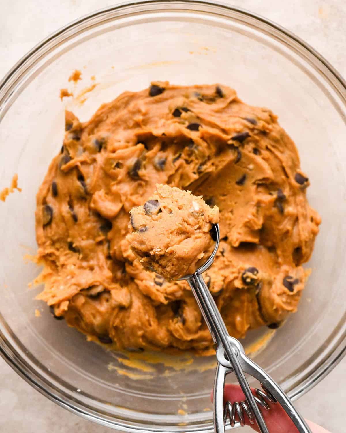 chilled brown butter pumpkin cookies dough in a glass bowl with a cookie scoop hovering over the bowl with a scoop of dough inside.