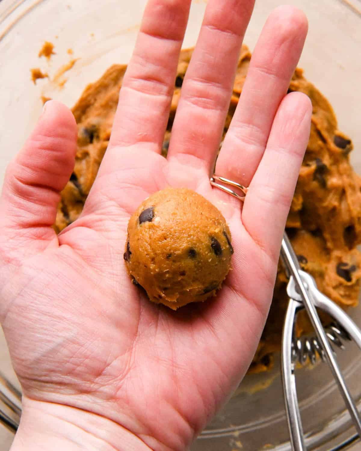 a hand rolling a ball of brown butter pumpkin cookie dough in nit