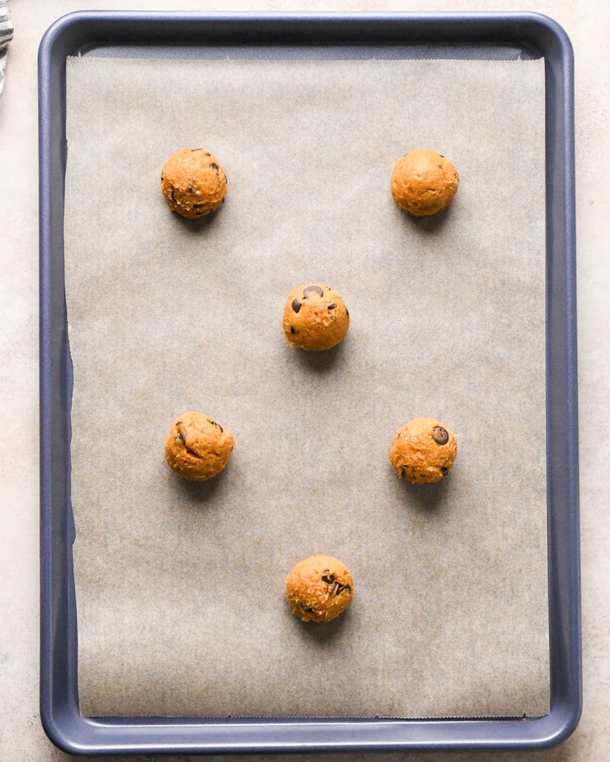 5 brown butter pumpkin chocolate chip cookie dough balls on a parchment lined baking sheet before baking