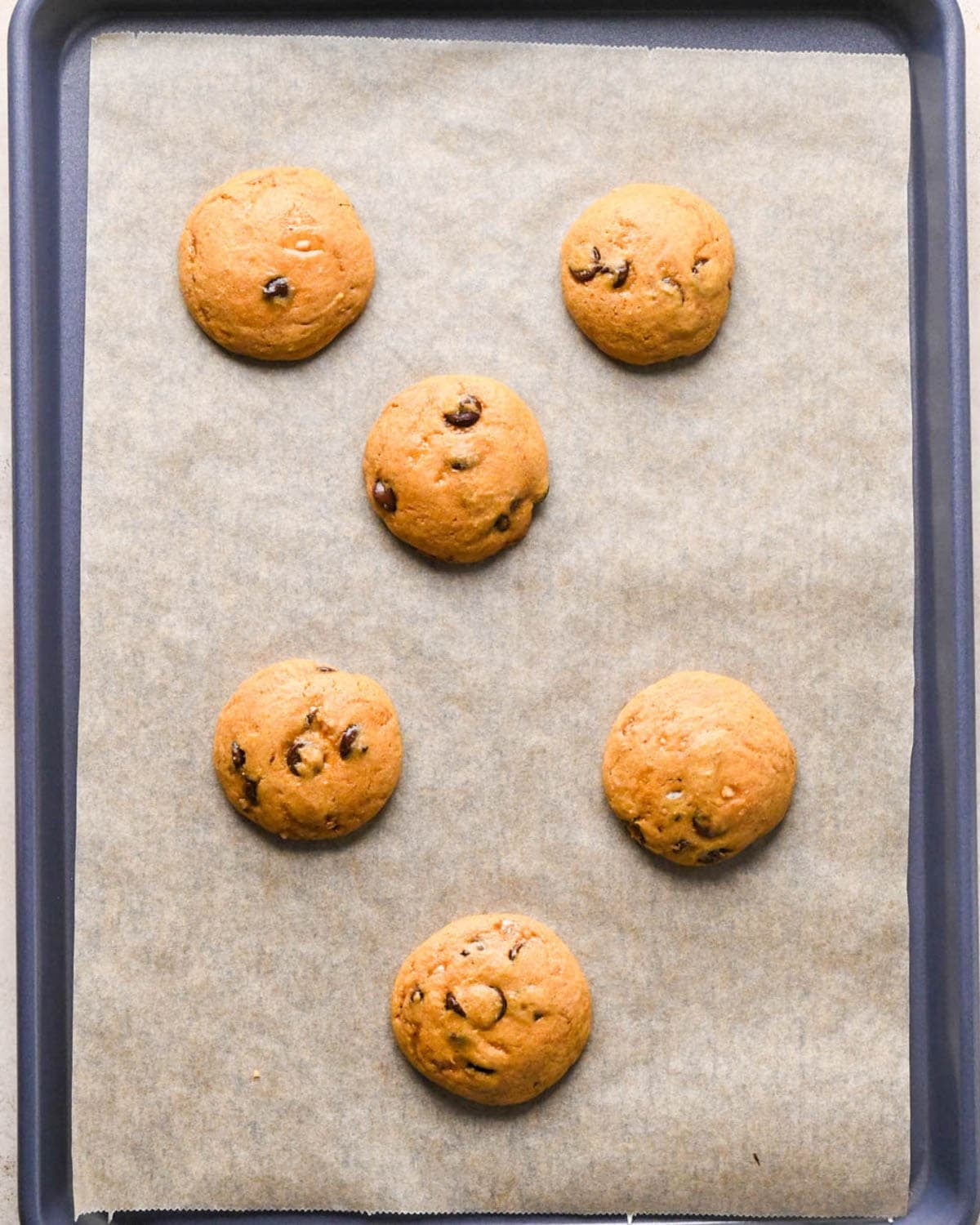 5 baked brown butter pumpkin cookies on a parchment lined baking sheet