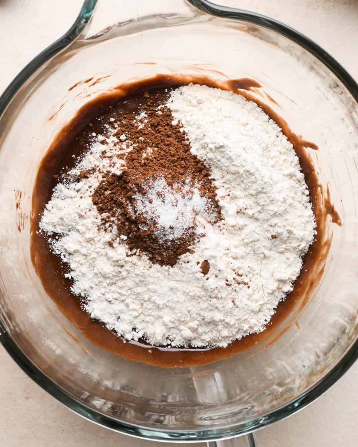 making brownie bites - flour, cocoa powder and salt added to the wet ingredient mixture in a glass mixing bowl