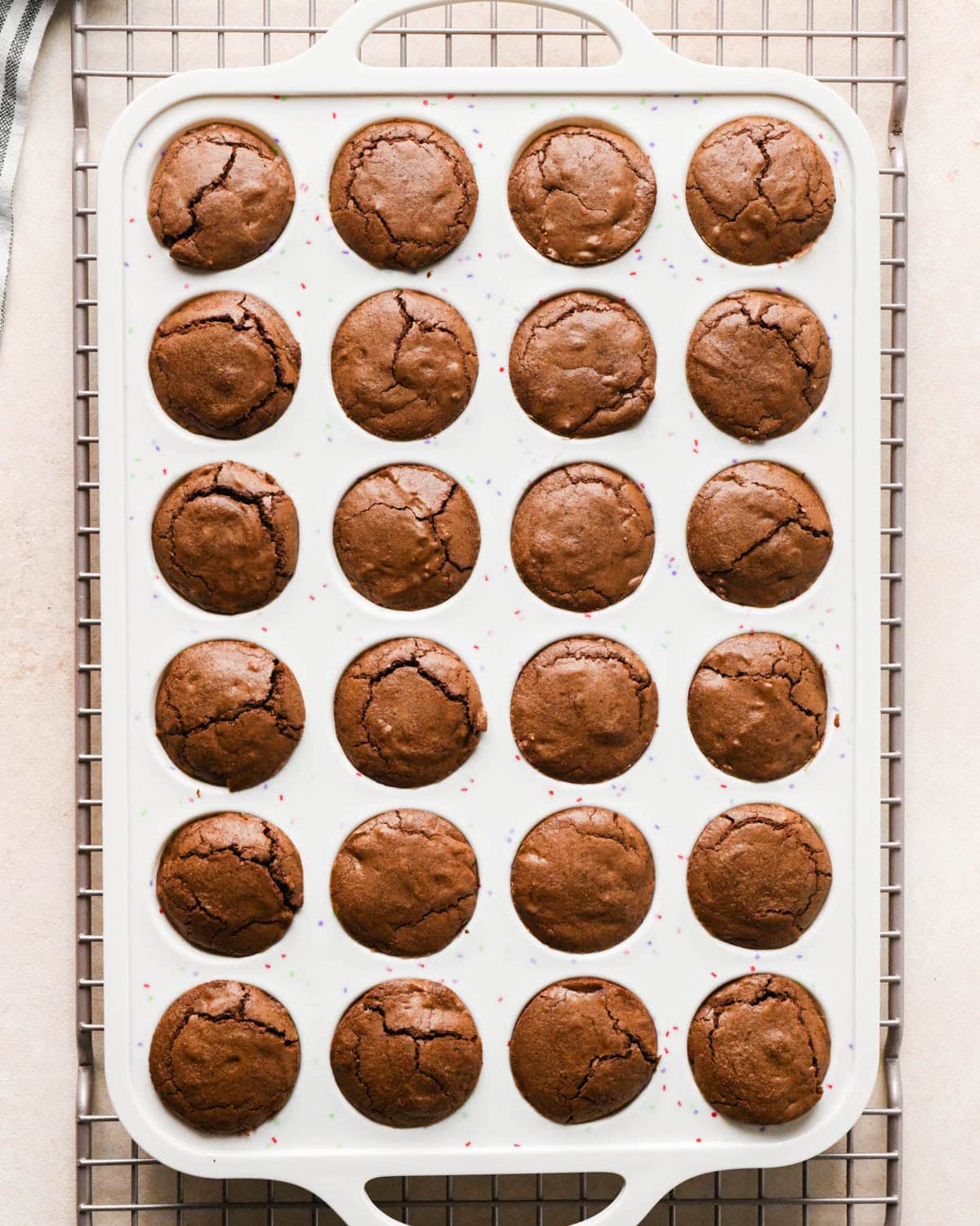 24 brownie bites in a white silicone mini muffin pan on a wire cooling rack after baking