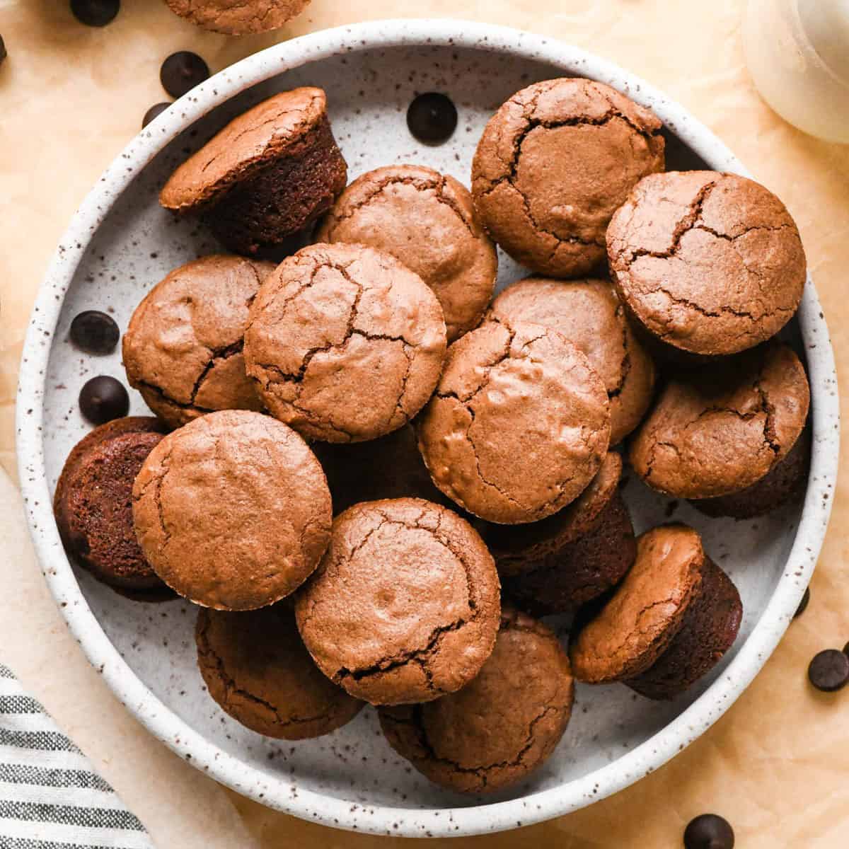 16 brownie bites on a round pottery plate on parchment paper with chocolate chips around it