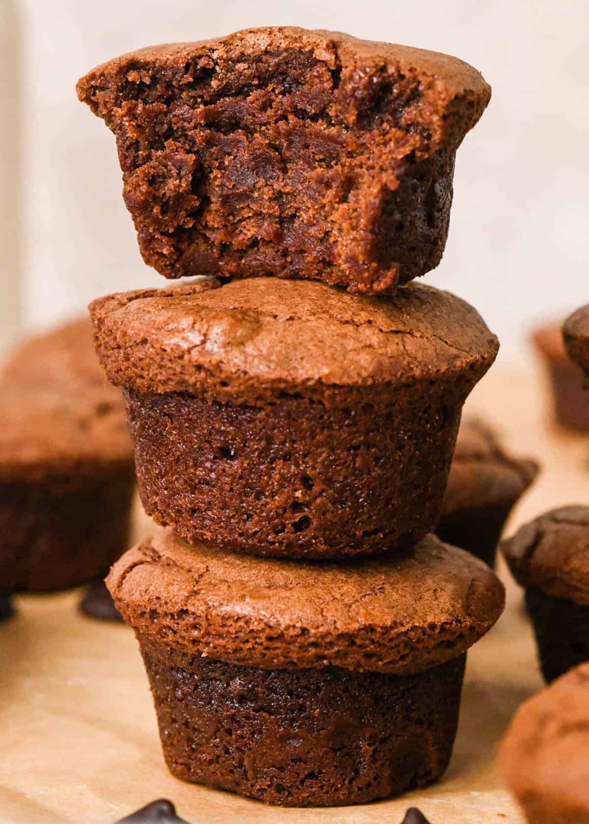 a stack of three brownie bites, the top one has a bite out of it showing it's fudgy texture, surrounded by more brownie bites and chocolate chips