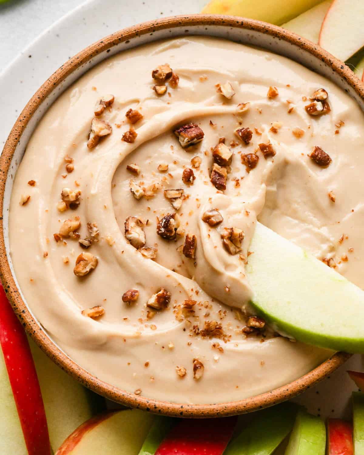 a green apple slice being dipped into a bowl of cream cheese apple dip surrounded by more red and green apple slices