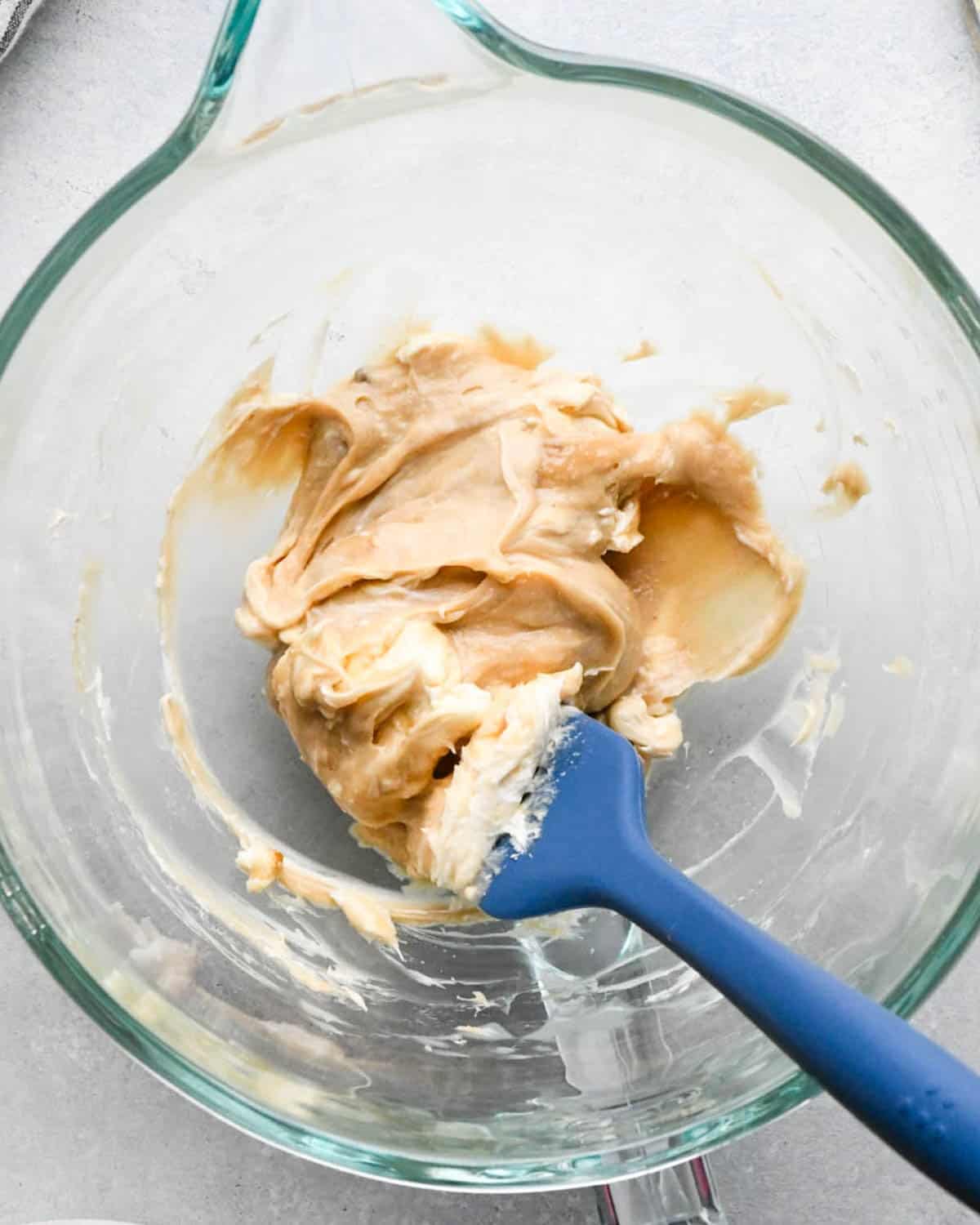 making caramel cream cheese apple dip - a blue spatula scraping down the sides of the bowl
