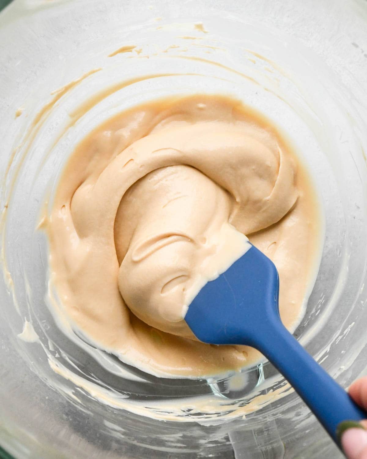 a blue spatula in cream cheese apple caramel dip in a glass mixing bowl showing it's smooth and creamy texture