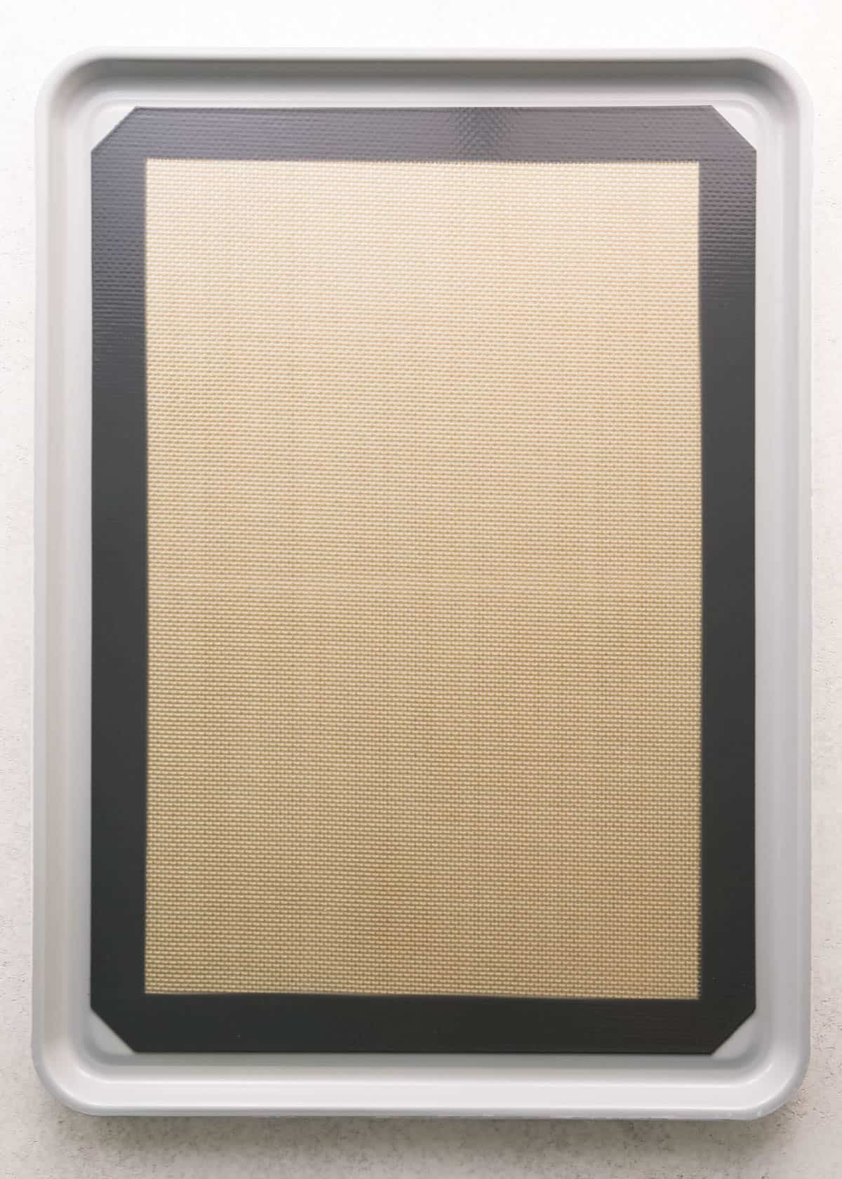 Overhead photo of a stainless steel baking sheet lined with a silicone baking mat and sitting on a countertop.