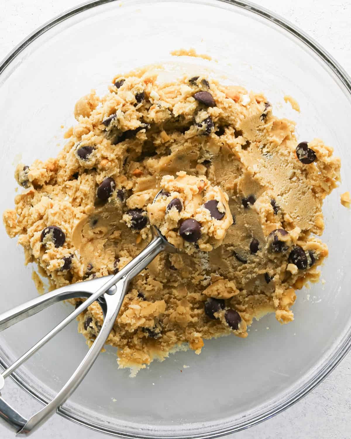 Making chocolate chip cashew cookies: overhead photo of a mixing bowl with prepared cookie dough. The cookie dough is being scooped with a cookie scoop.