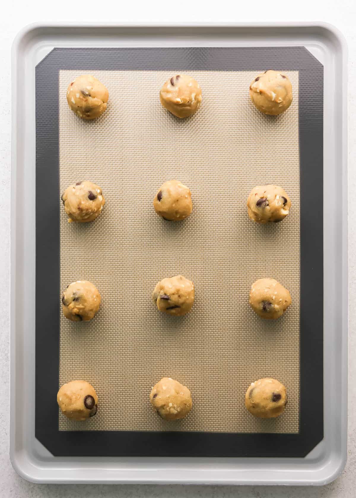 Making chocolate chip cashew cookies: overhead photo of 12 balls of cookie dough scooped, rolled, and placed onto a baking sheet on a countertop.