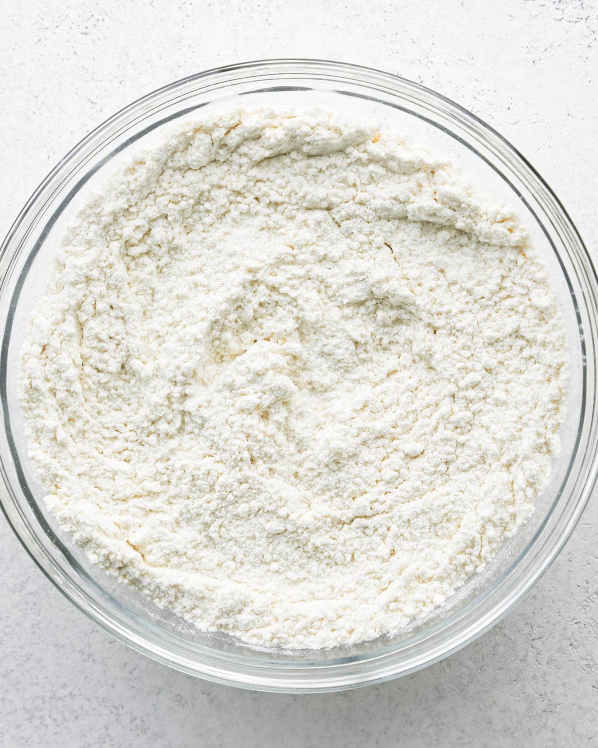 Making chocolate chip cashew cookies: overhead photo of the dry ingredients for cashew cookies in a large clear mixing bowl and mixed together.