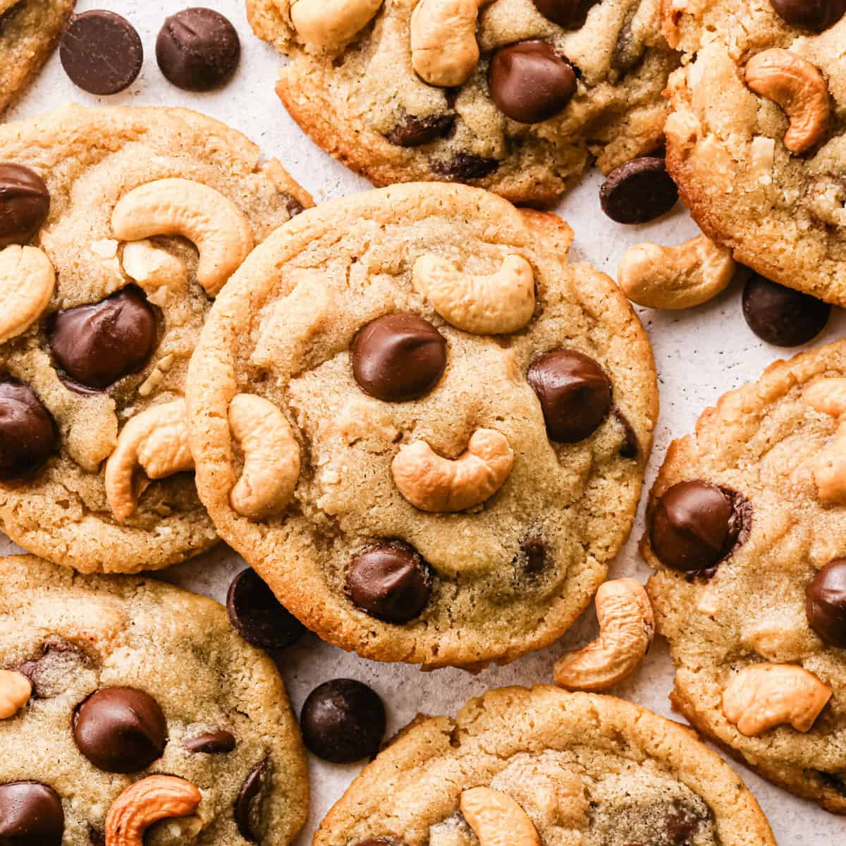 Overhead photo of golden-brown chocolate chip cashew cookies on parchment paper, studded with large chocolate chips and whole roasted cashews, with a few loose chocolate chips and cashews scattered around the cookies.